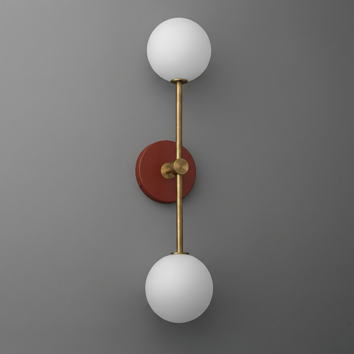 Raw brass double globe sconce with brick red circular backplate and frosted white glass shades. - SCONCE MODEL NO. 9776