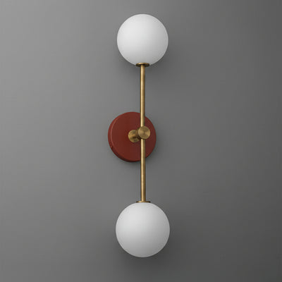 Raw brass double globe sconce with brick red circular backplate and frosted white glass shades. - SCONCE MODEL NO. 9776