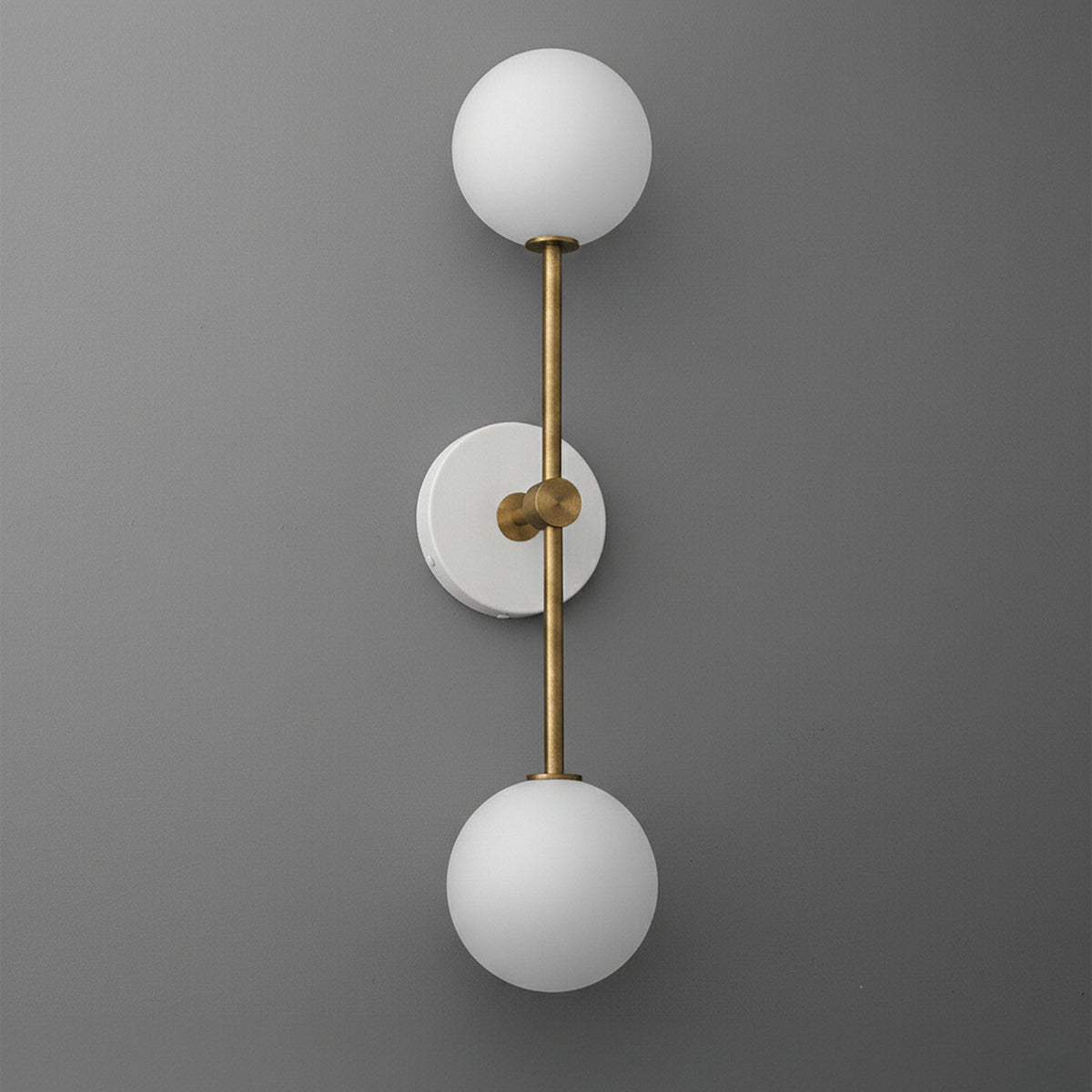 Wall sconce with double white glass globes and raw brass vertical rod mounting on gray wall. - SCONCE MODEL NO. 9776