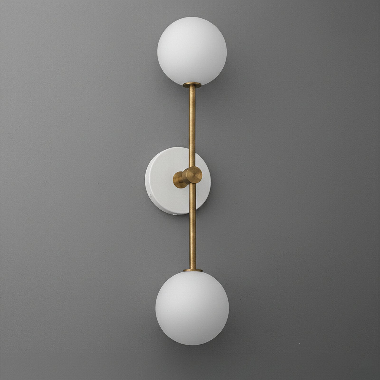 Wall sconce with double white glass globes and raw brass vertical rod mounting on gray wall. - SCONCE MODEL NO. 9776