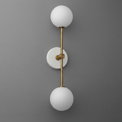 Wall sconce with double white glass globes and raw brass vertical rod mounting on gray wall. - SCONCE MODEL NO. 9776