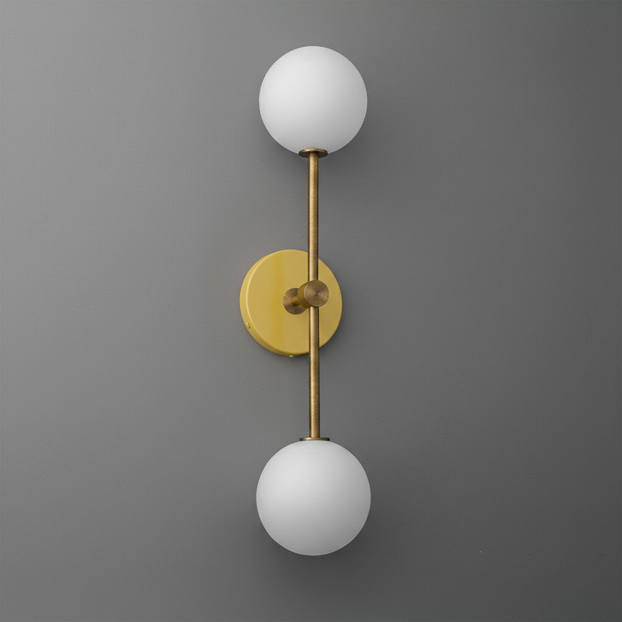 Raw brass double globe wall sconce with frosted white glass shades on gray background. - SCONCE MODEL NO. 9776