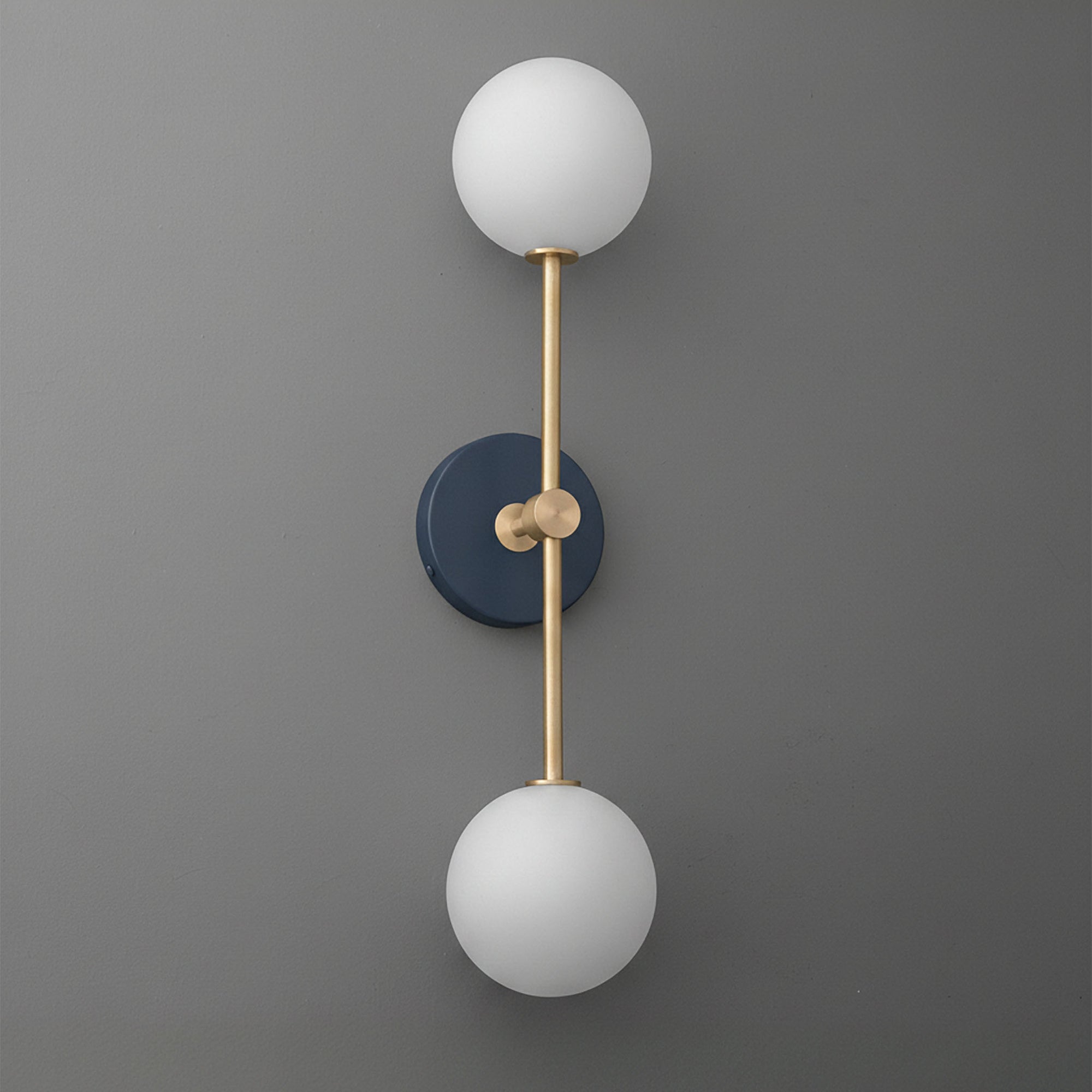 Wall sconce with raw brass finish, two frosted white glass globes, and a dark blue circular backplate. - SCONCE MODEL NO. 9776