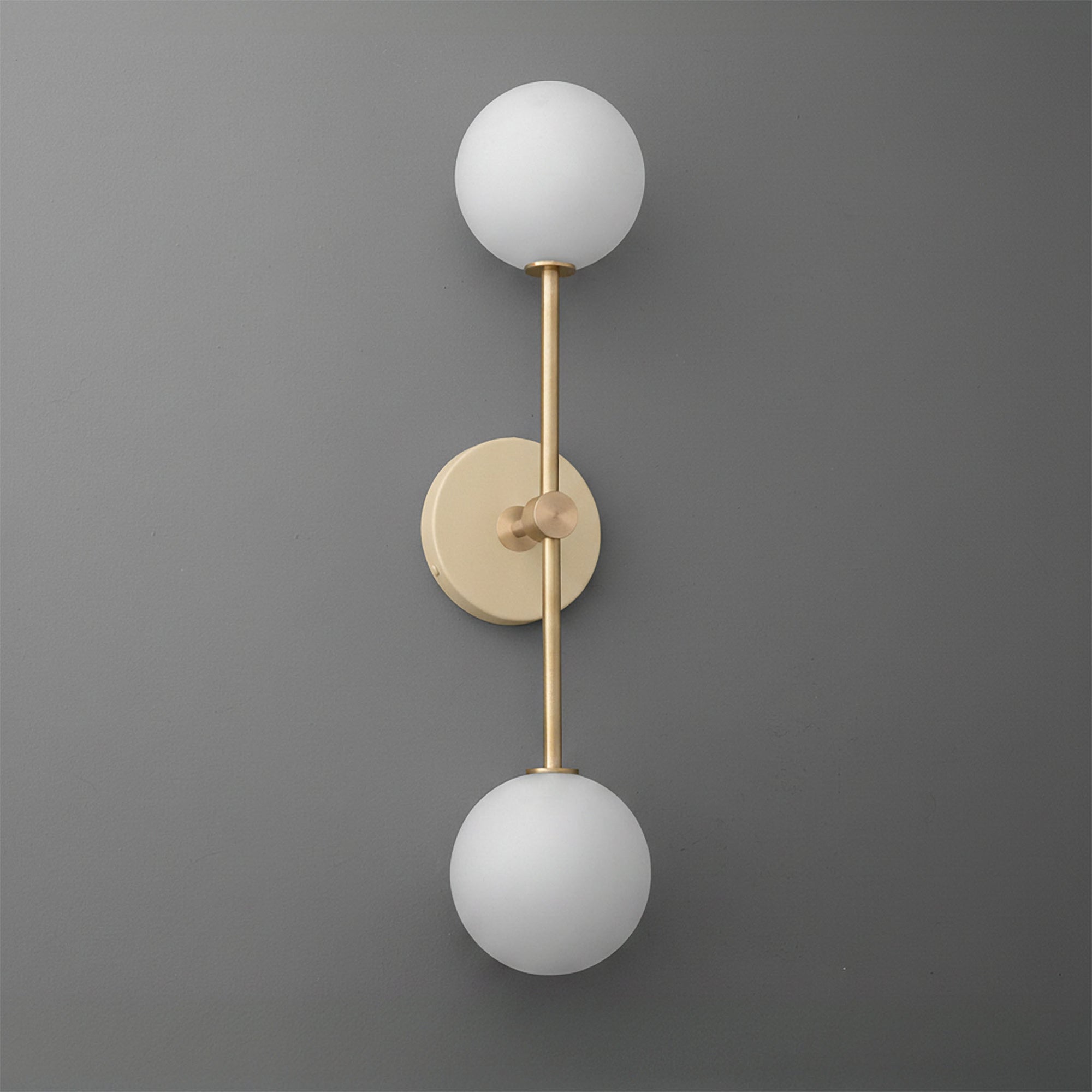 Wall sconce with raw brass finish and two white frosted glass globes on a gray background. - SCONCE MODEL NO. 9776