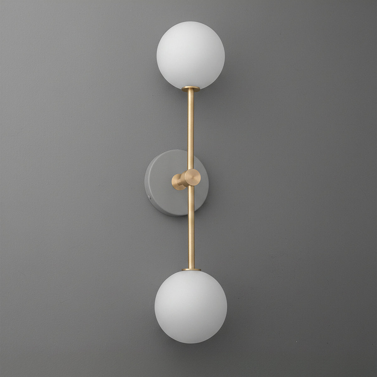 Modern double-globe wall sconce with matte brass finish and frosted white glass shades on gray wall. - SCONCE MODEL NO. 9776