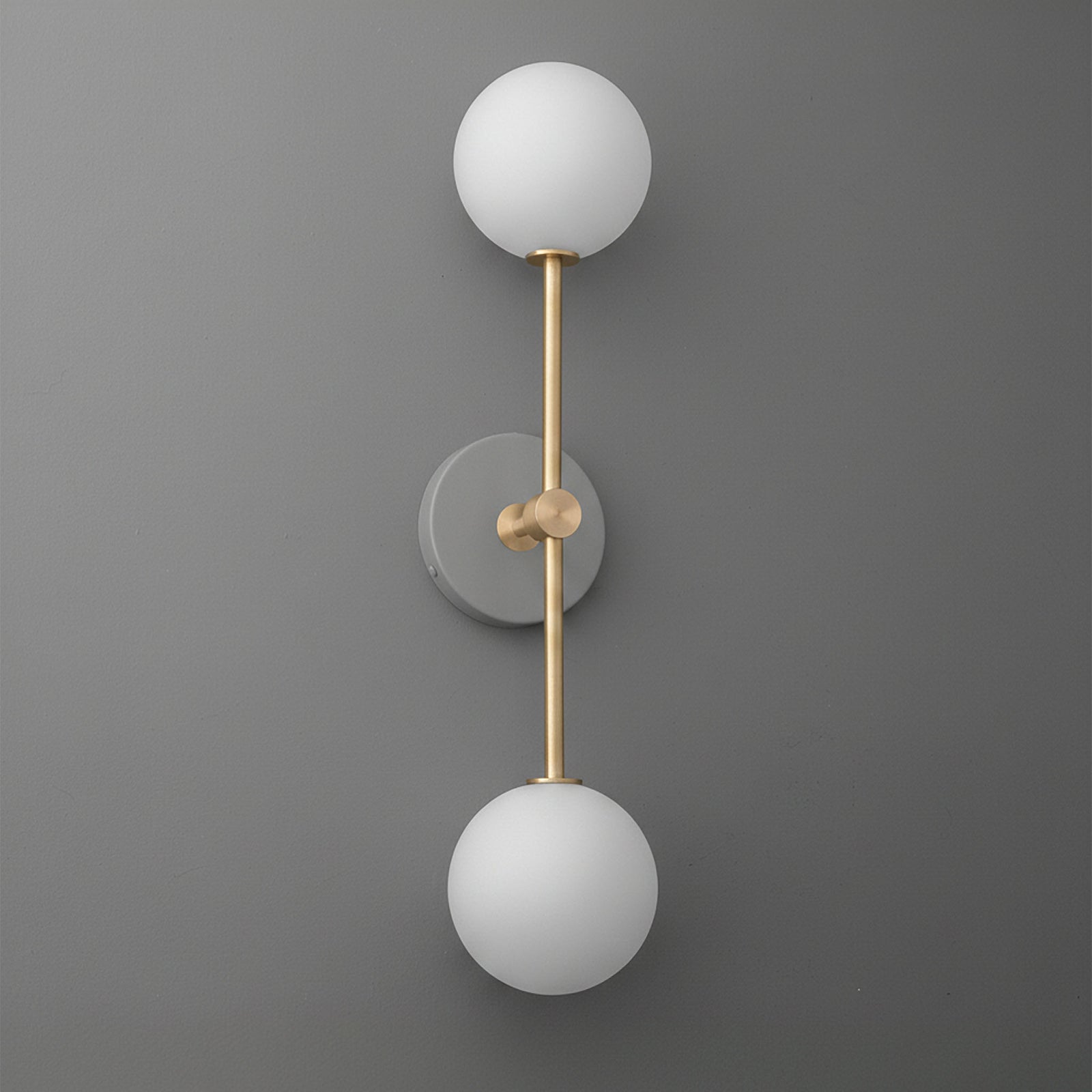 Modern double-globe wall sconce with matte brass finish and frosted white glass shades on gray wall. - SCONCE MODEL NO. 9776