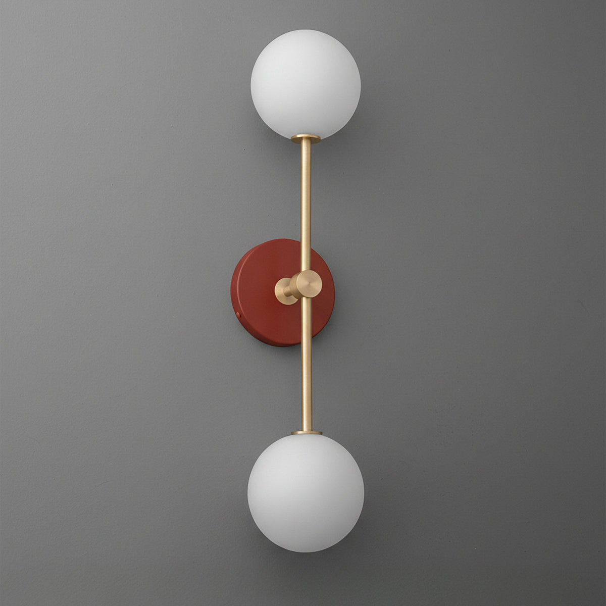 Raw brass double globe sconce with brick red round backplate on gray wall. - SCONCE MODEL NO. 9776