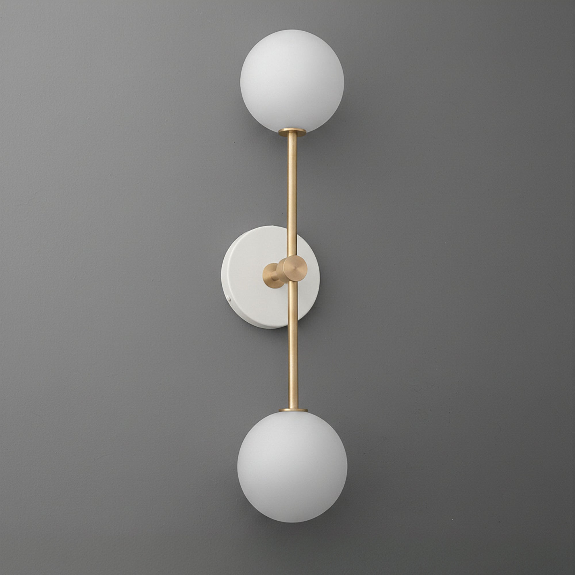 Modern double globe wall sconce with raw brass finish and frosted white glass shades on matte gray wall. - SCONCE MODEL NO. 9776