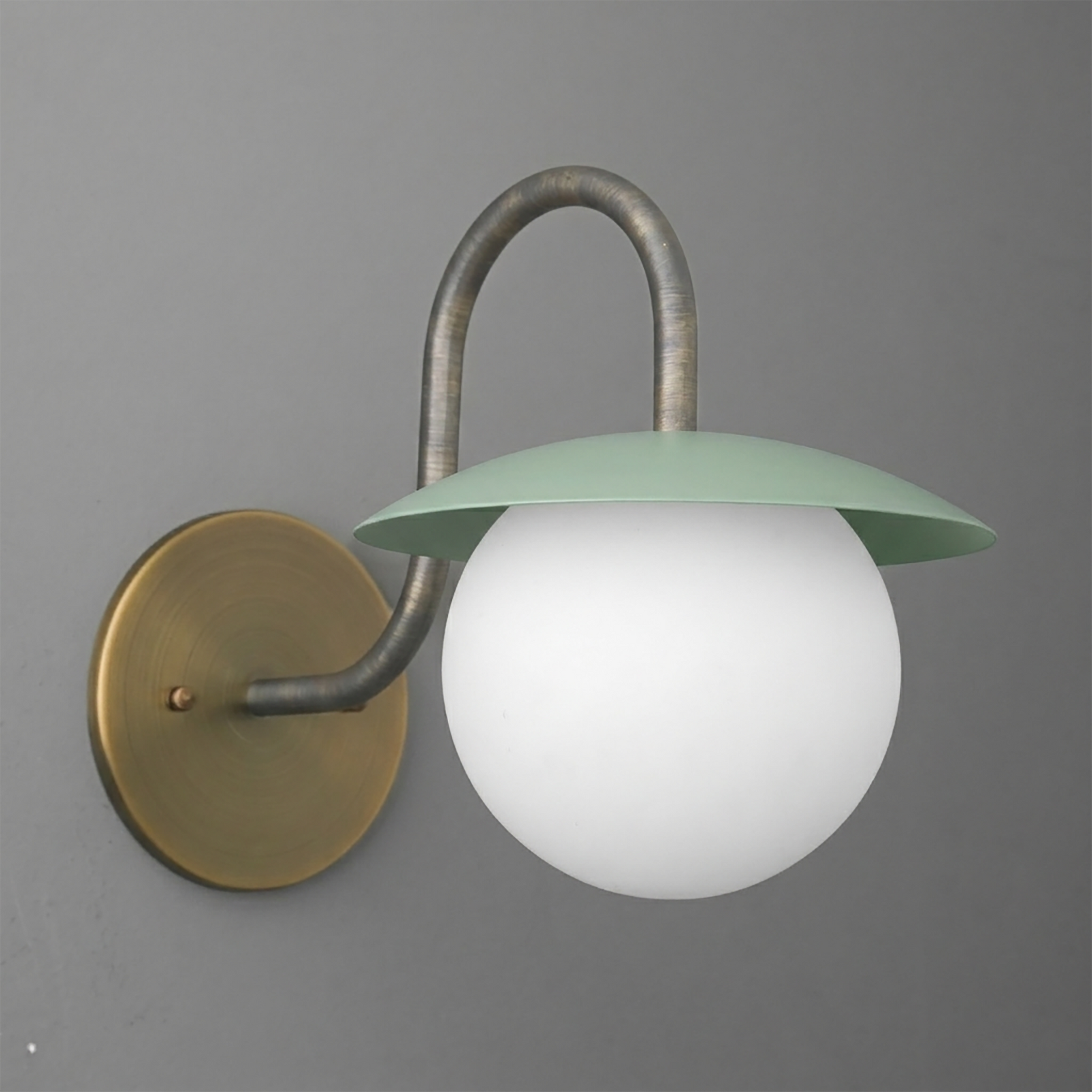 Wall sconce with brass round base, curved dark metal arm, and matte green shade over frosted white glass globe bulb. - SCONCE MODEL NO. 2206