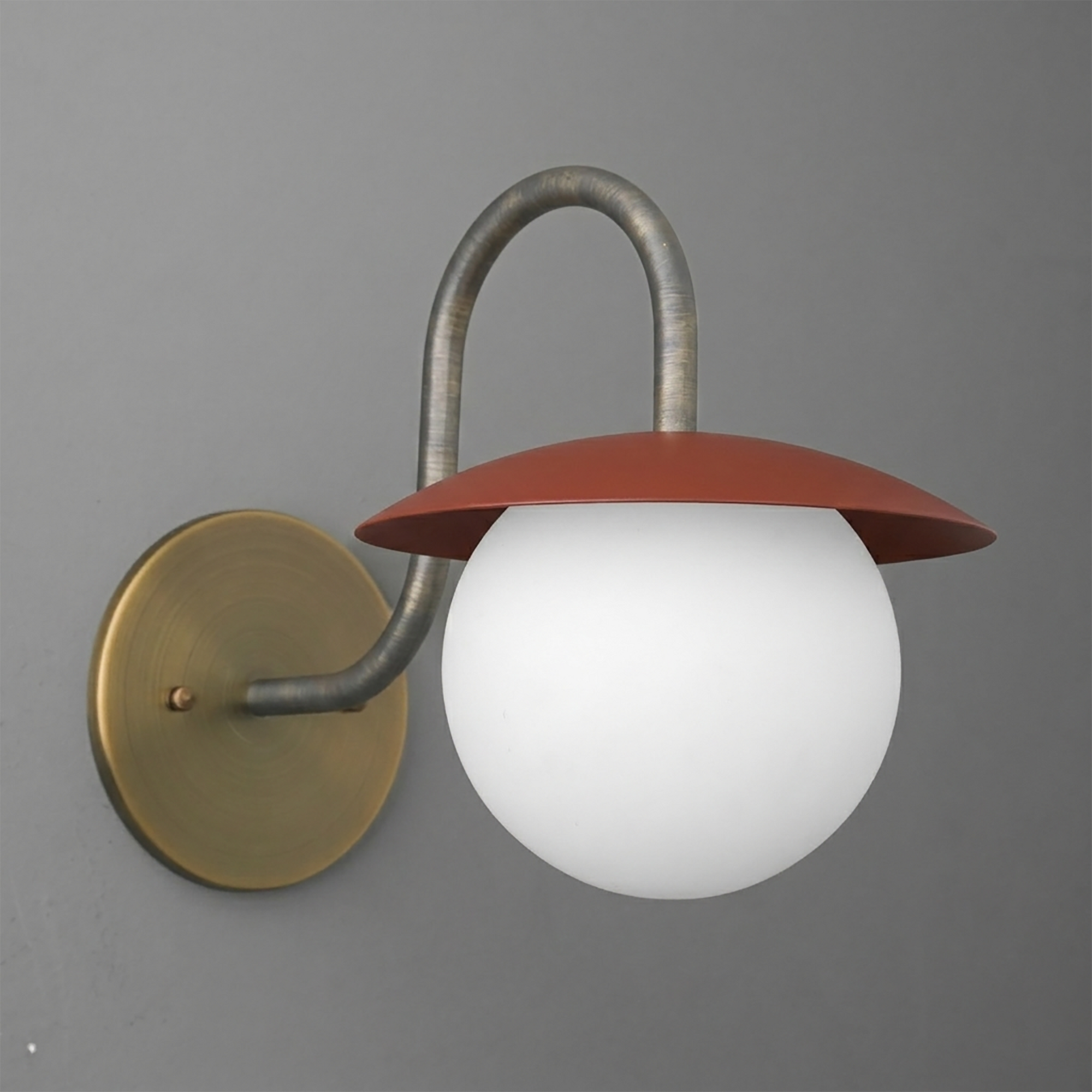 Wall sconce with brass round base, curved metal arm, and frosted white globe shade topped by a rust-red metal cap. - SCONCE MODEL NO. 2206