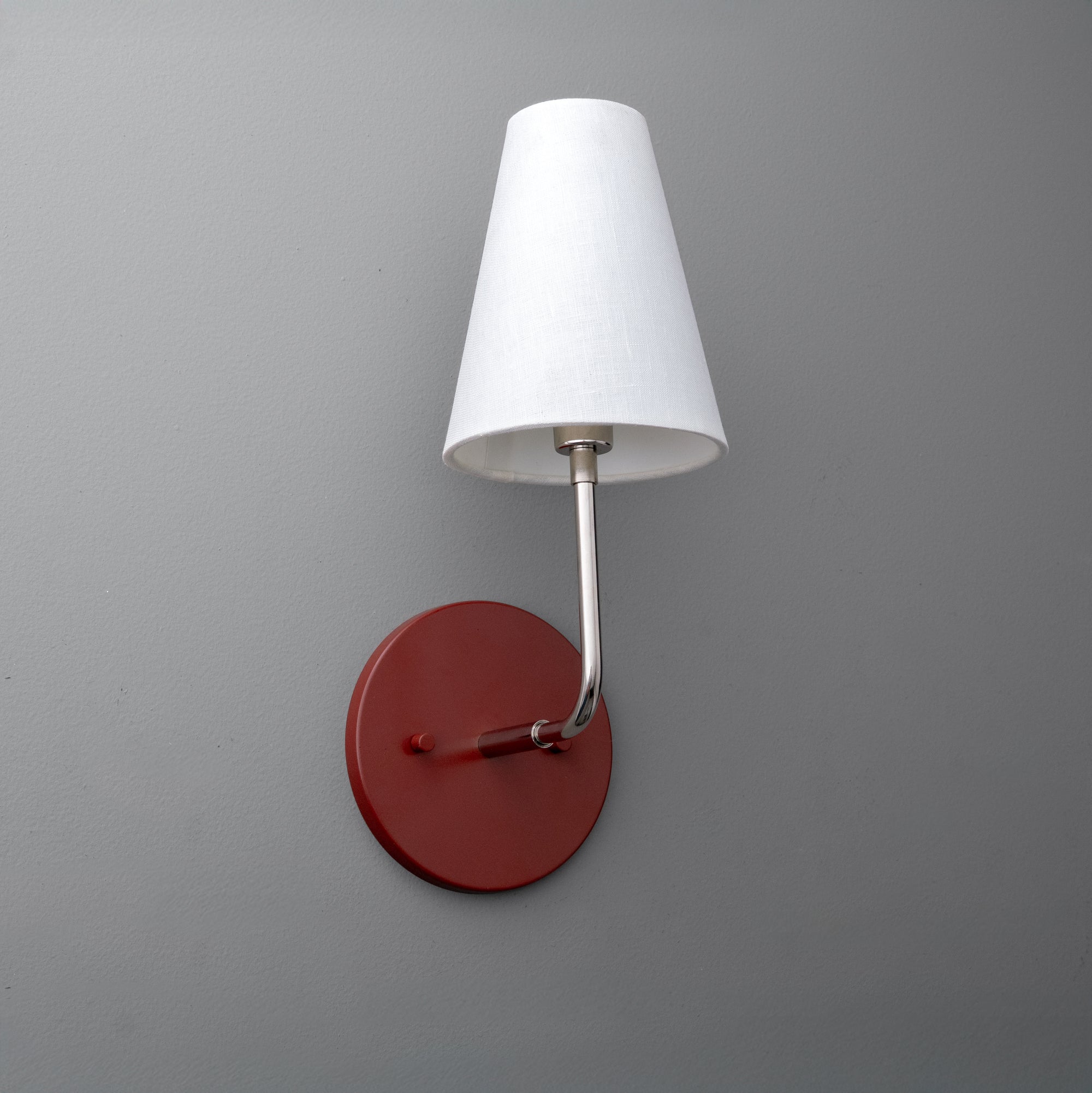 Wall sconce with polished nickel arm, brick red circular base, and white fabric tapered shade. - SCONCE MODEL NO. 3928