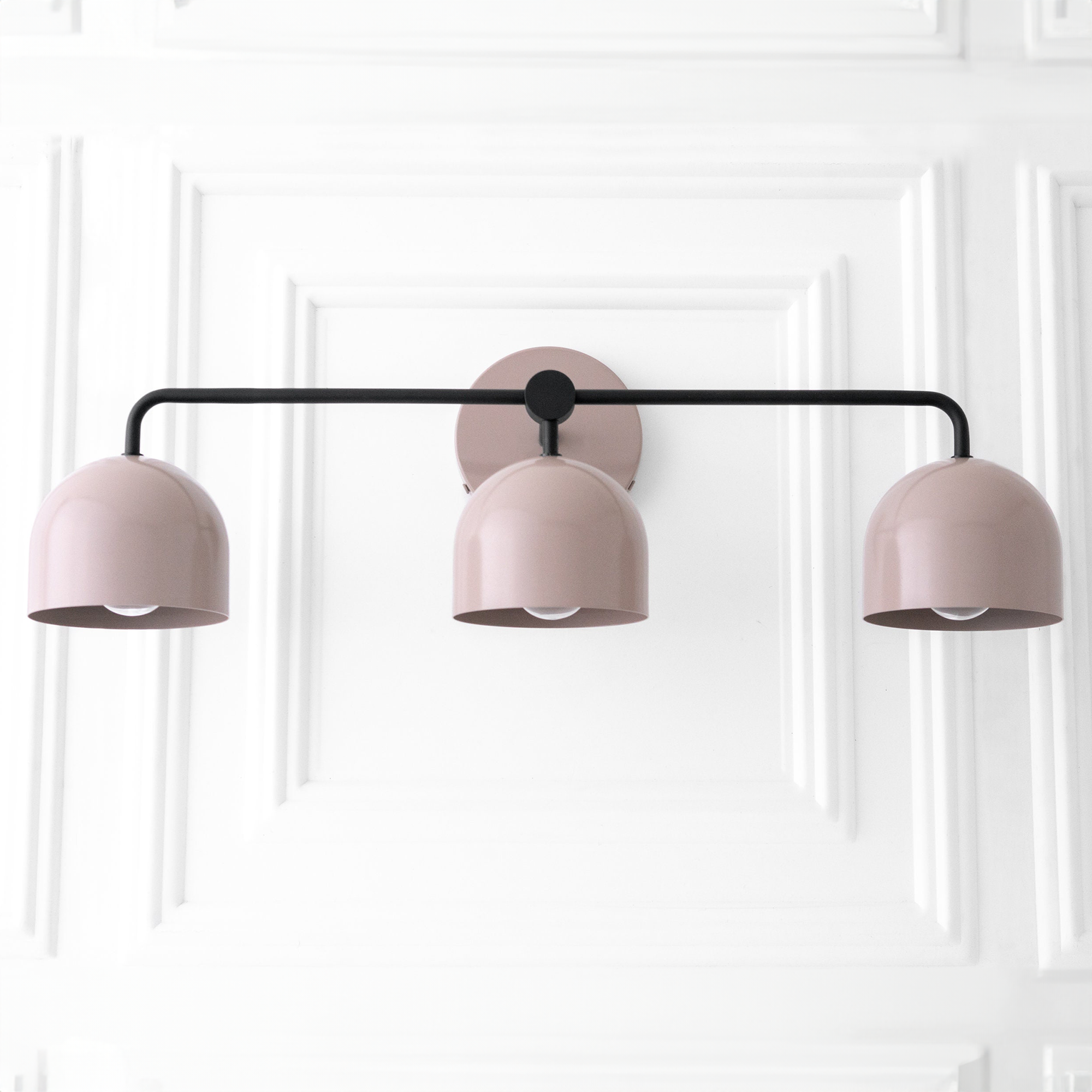 Mid-century modern vanity light with three muted pink dome shades and a matte black horizontal rod mounted on a round base. - VANITY LIGHT MODEL NO. 7456