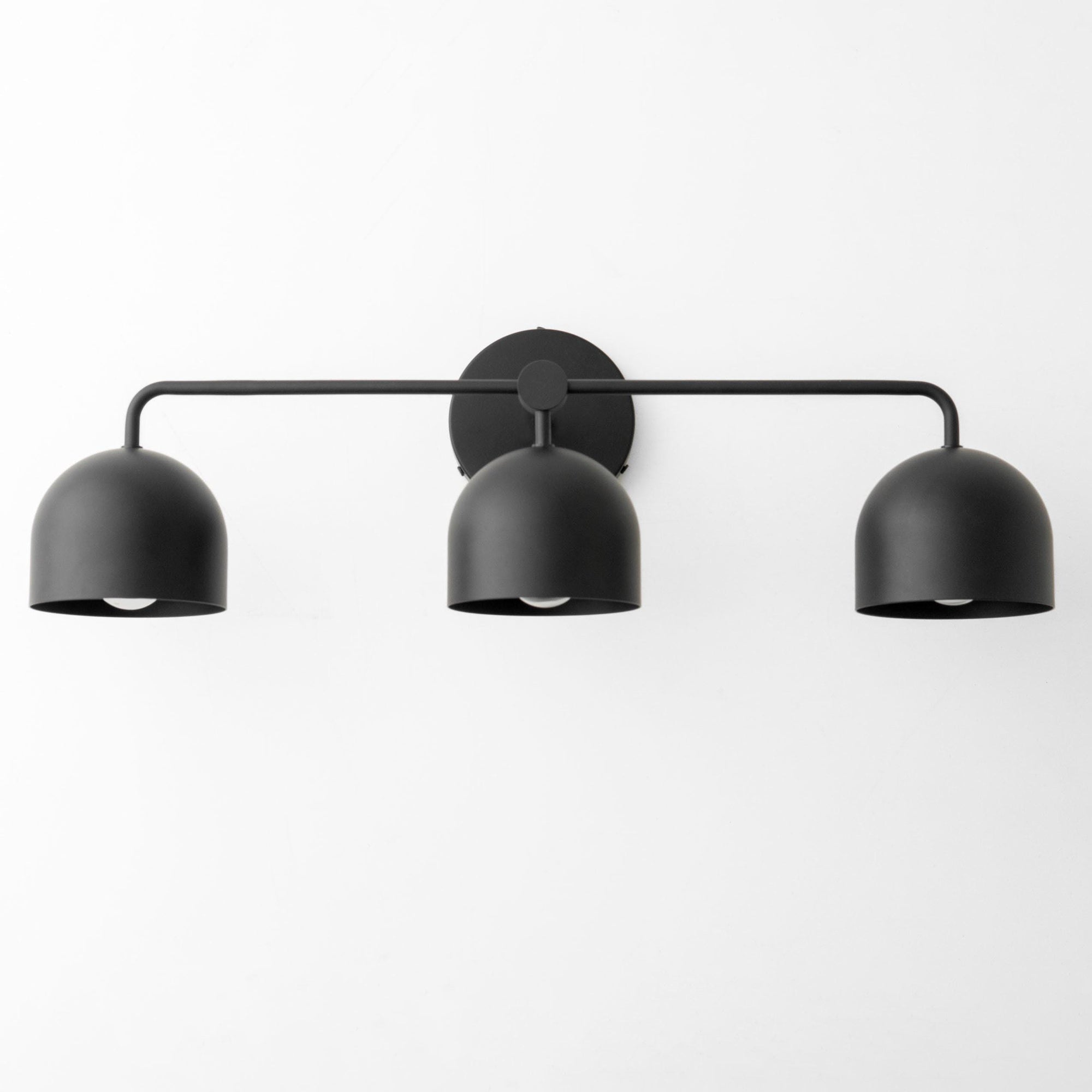 Black metal three-bulb vanity light with dome-shaped shades and a horizontal bar mount. - VANITY LIGHT MODEL NO. 7456