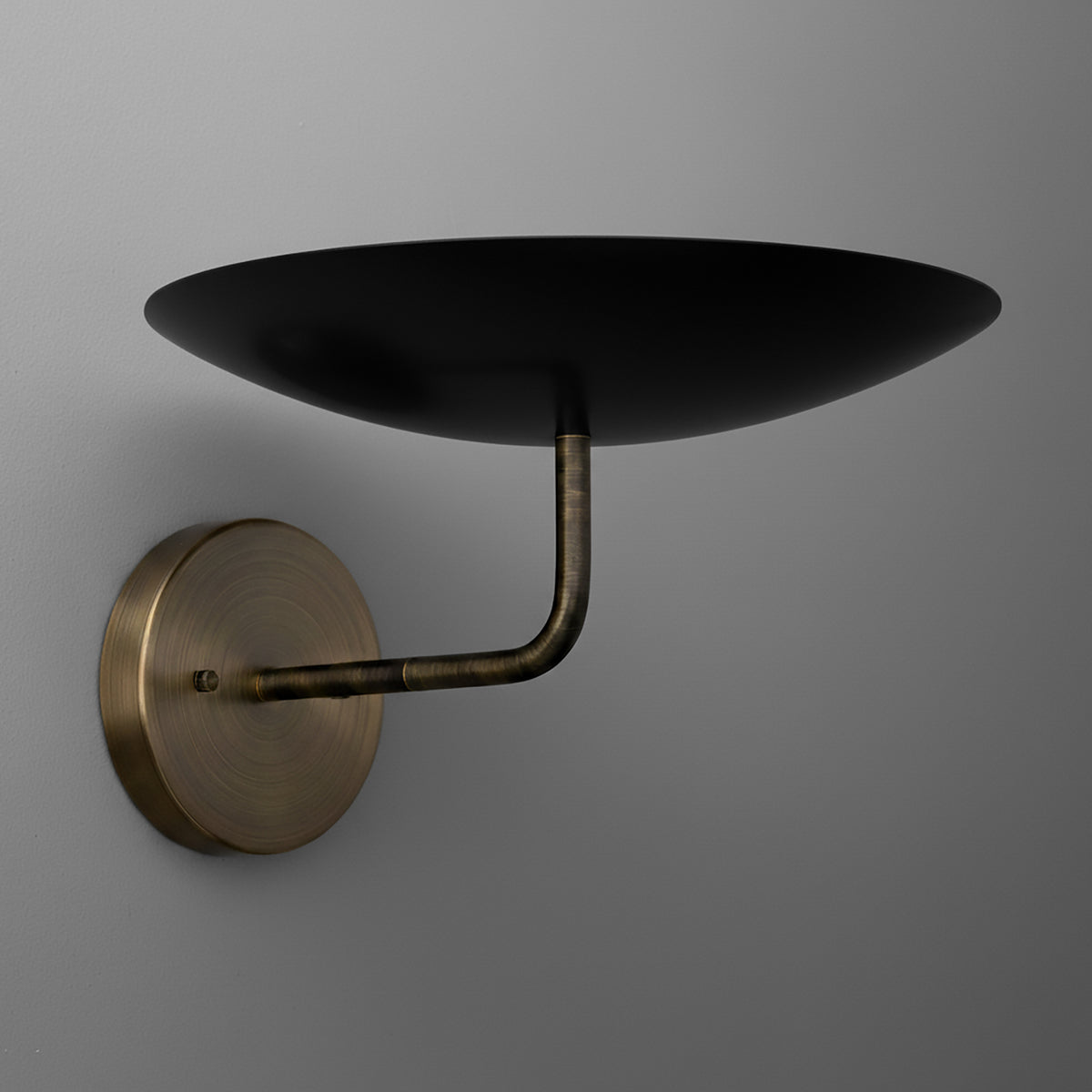Wall sconce with aged brass finish and curved arm supporting a wide black metal shade. - SCONCE MODEL NO. 1504