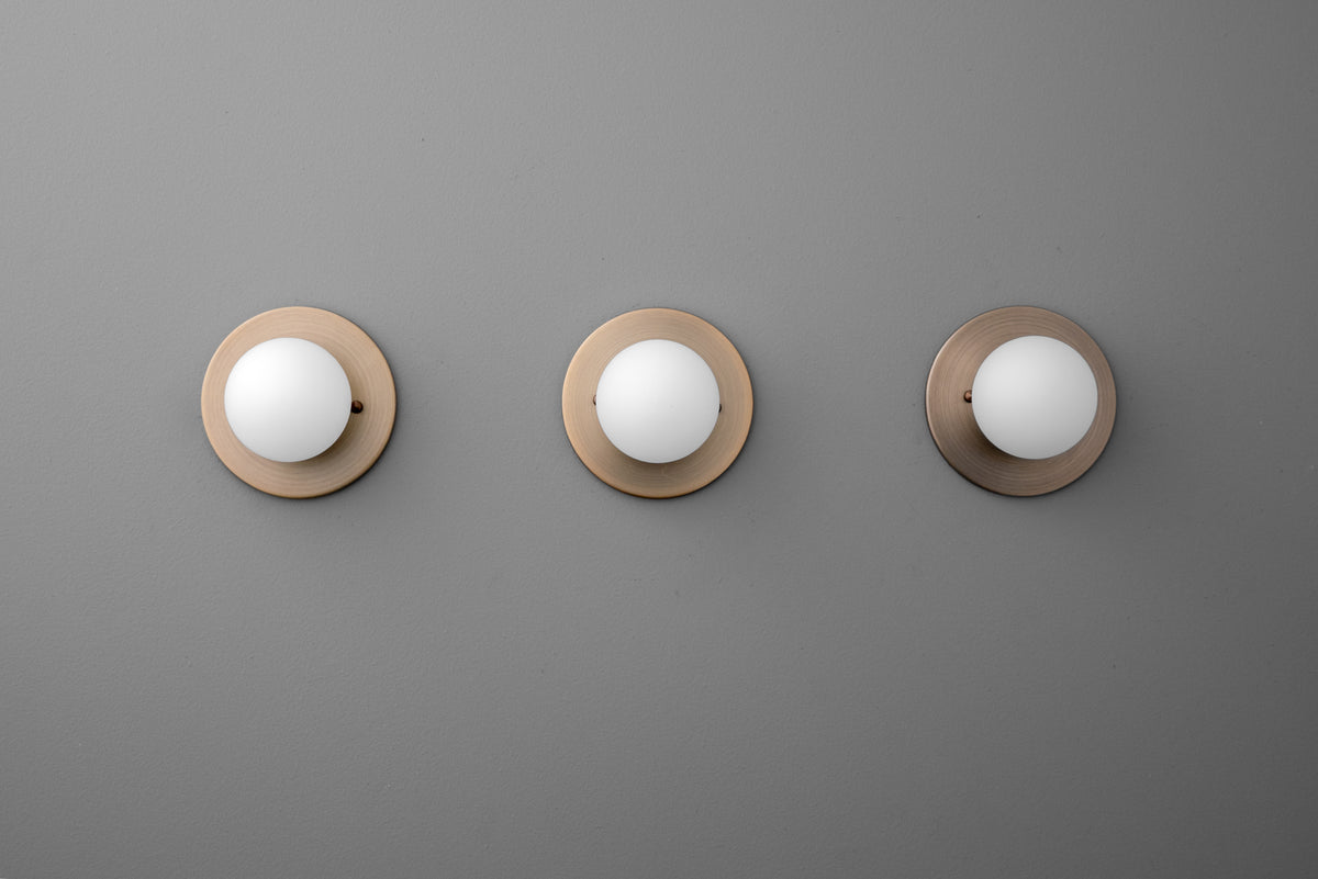 Three antique brass sconces with 3 inch frosted globe shades mounted on gray wall. - Sconce Model No. 5206