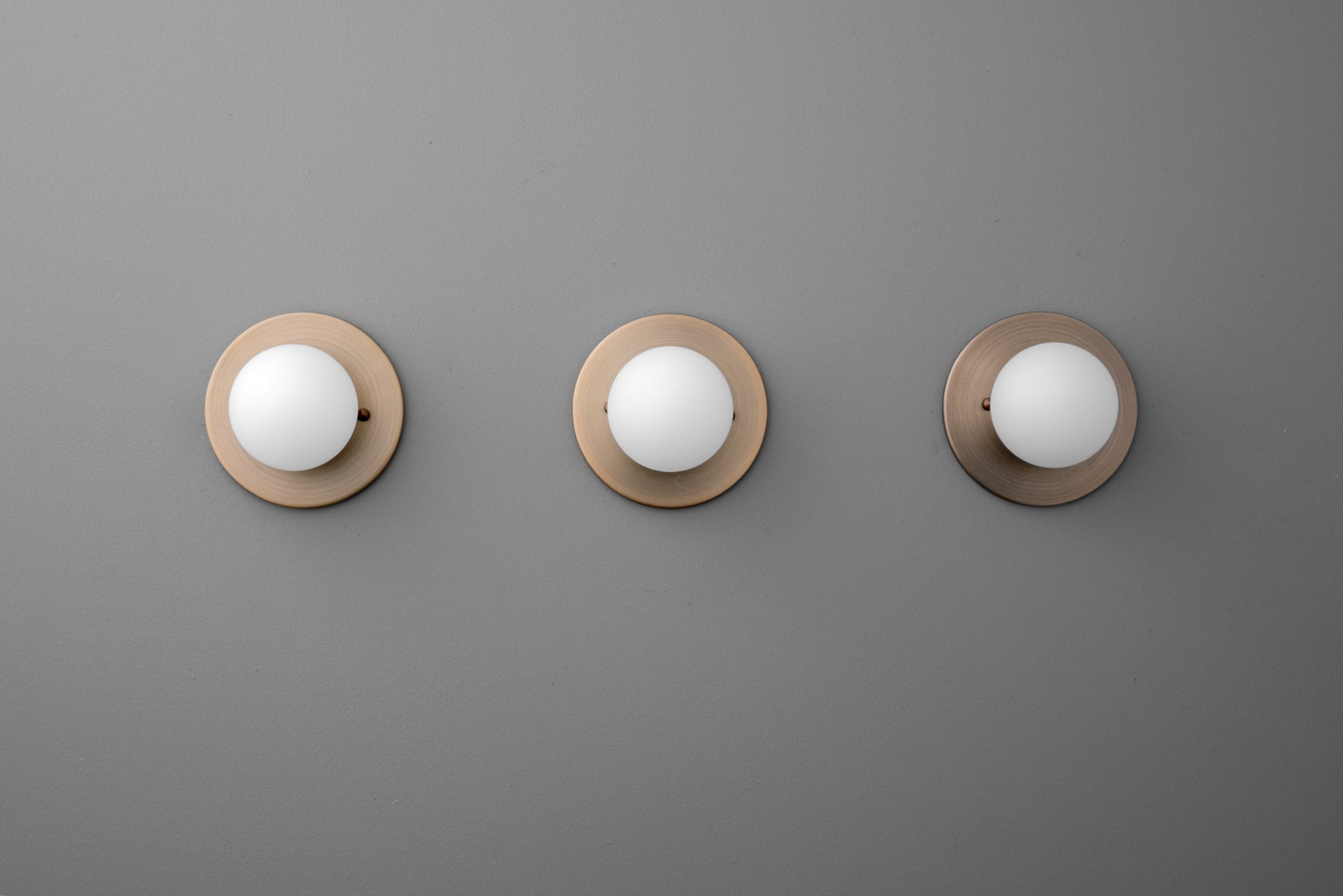 Three antique brass sconces with 3 inch frosted globe shades mounted on gray wall. - Sconce Model No. 5206