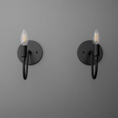 Pair of matte black metal wall sconces with minimalist curved arms and exposed candle-style bulbs. - SCONCE MODEL NO. 7321