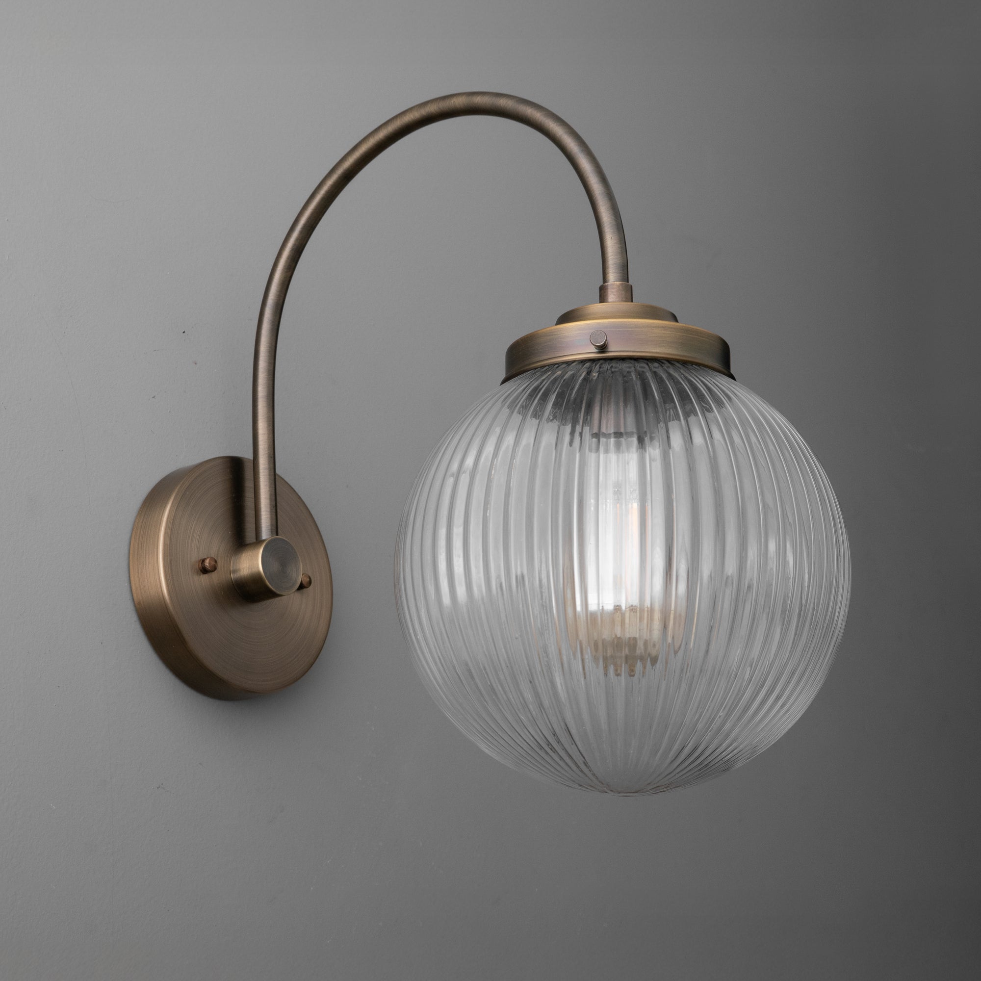 Antique brass wall sconce with ribbed clear glass globe shade and curved arm mount. - SCONCE MODEL NO. 8763