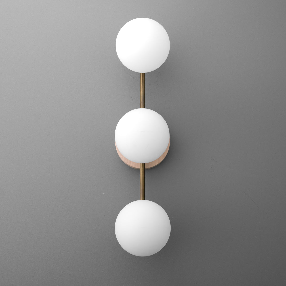 Modern wall sconce with three frosted white glass globes arranged vertically on a brushed brass rod and circular base. - SCONCE MODEL NO. 6089