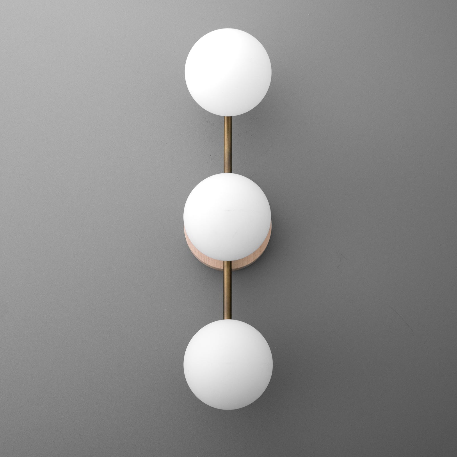 Modern wall sconce with three frosted white glass globes arranged vertically on a brushed brass rod and circular base. - SCONCE MODEL NO. 6089