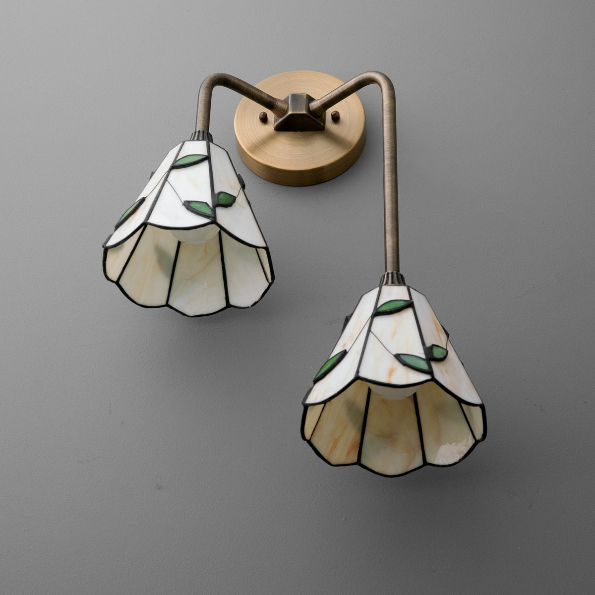 Two-bulb wall sconce with bronze metal arms and white stained glass shades featuring green leaf accents. - SCONCE MODEL NO. 8593