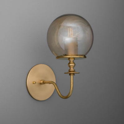 Brushed brass wall sconce with curved arm and clear glass globe shade featuring exposed filament bulb. - SCONCE MODEL NO. 1029