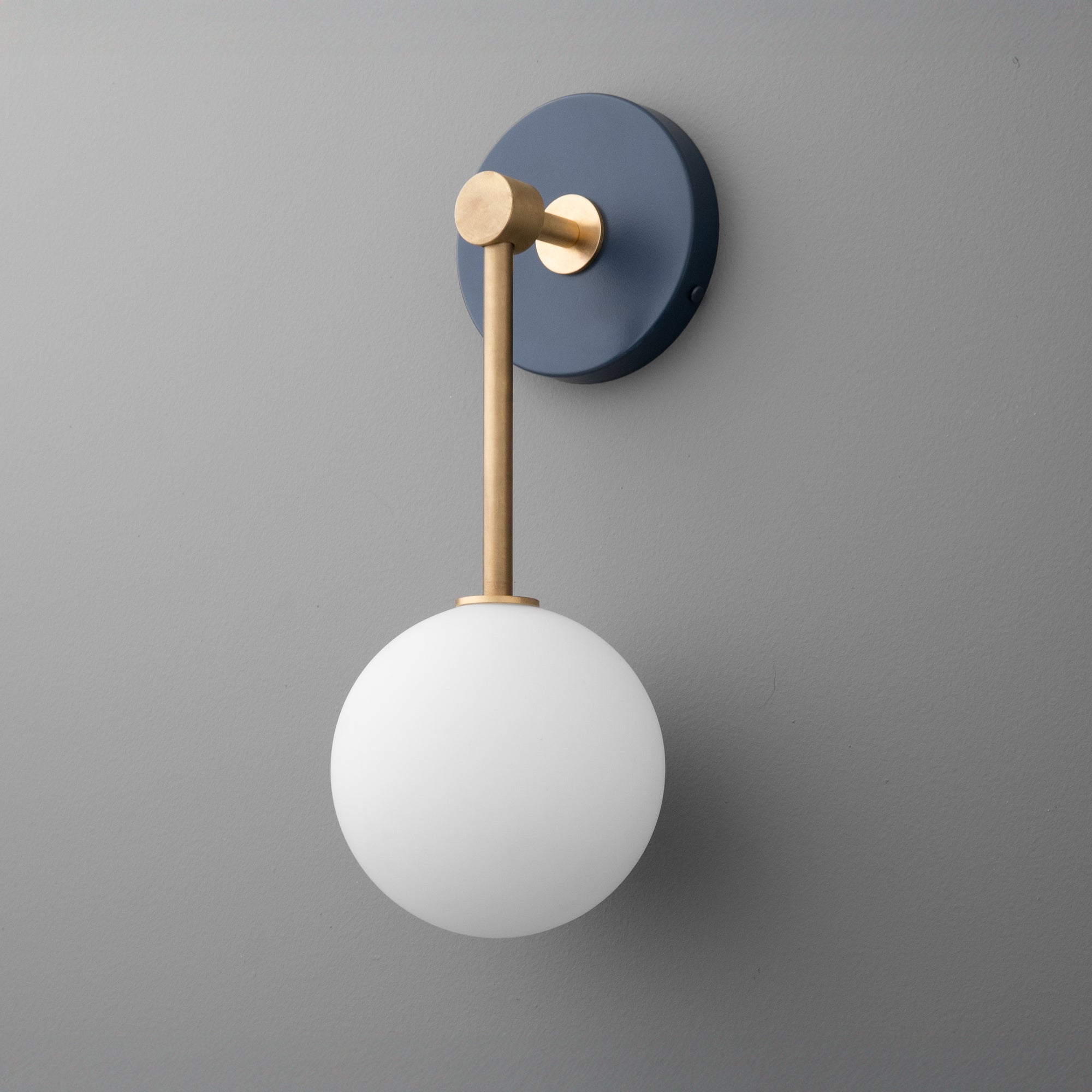 Wall sconce with a matte black circular base, raw brass arm, and a white frosted globe shade. - Sconce Model No. 5999