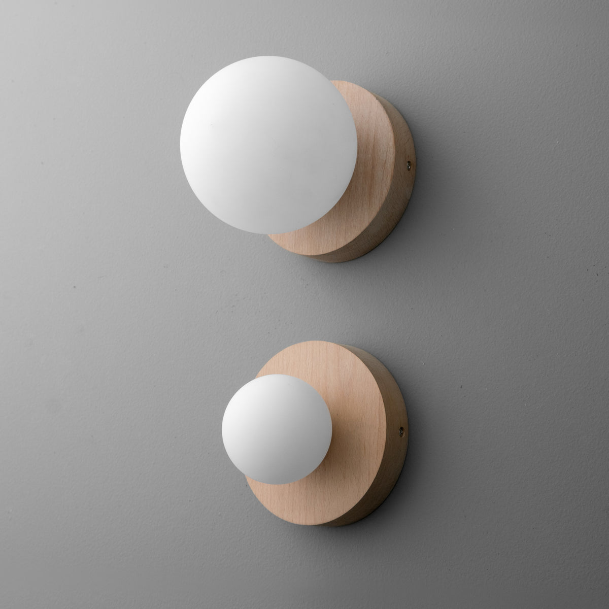 Two modern wall sconces with round frosted glass globes and light beechwood bases on a gray wall. - SCONCE MODEL NO. 4943