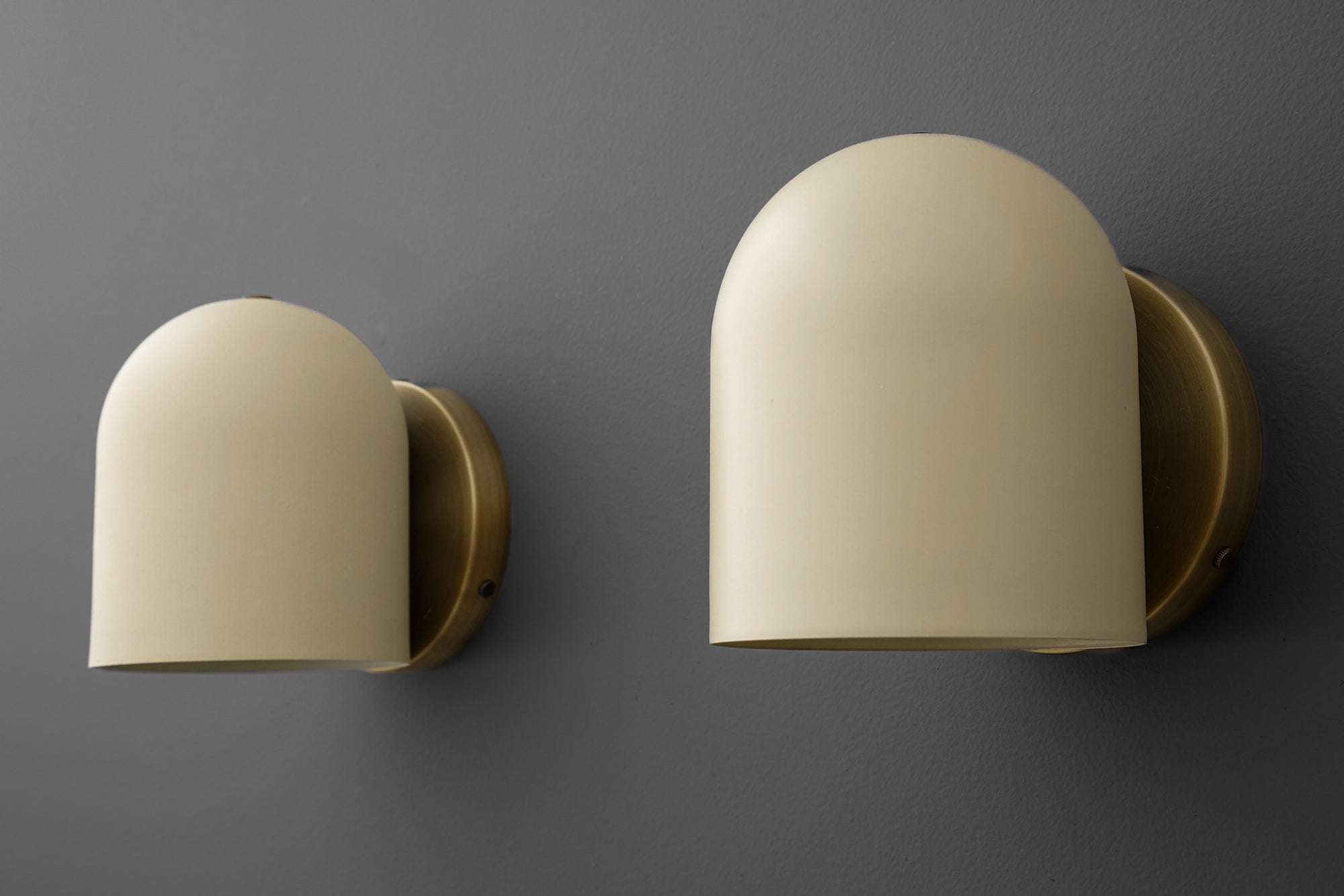 Matte cream modern dome-shaped wall sconces with brass mounting plates on gray wall. - SCONCE MODEL NO. 2424