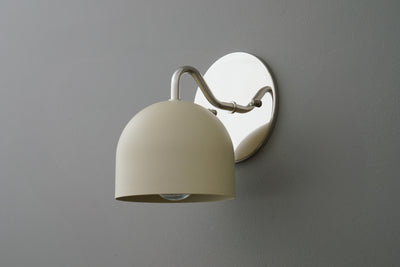 Wall sconce with cream-colored dome shade and polished nickel curved arm and backplate against gray wall. - SCONCE MODEL NO. 9436