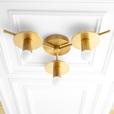 Raw brass flush mount chandelier with three exposed bulbs and minimalist arms on white ceiling panel. - CHANDELIER MODEL NO. 9526