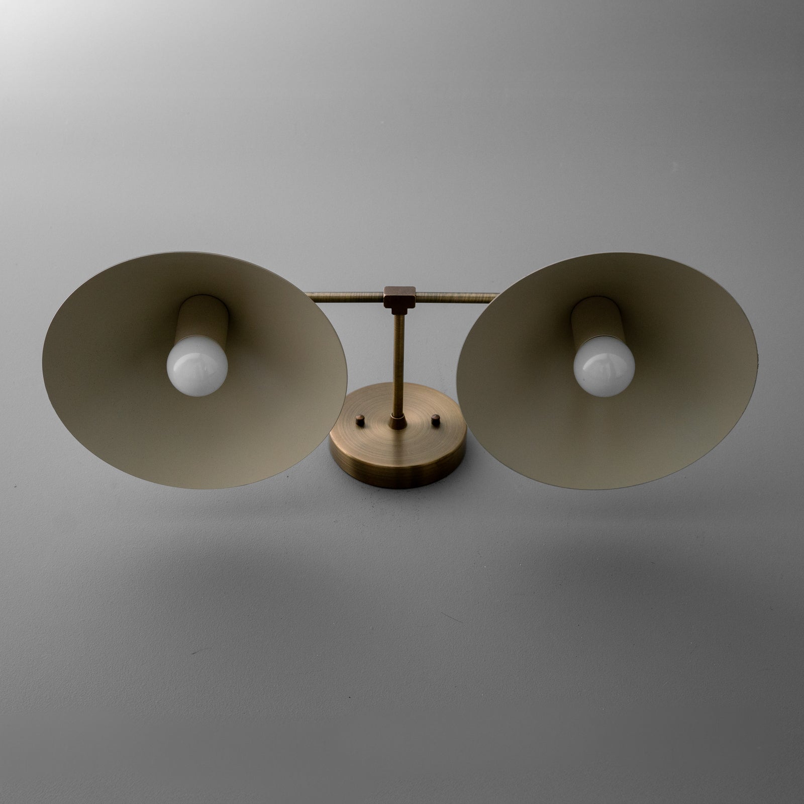 View from below of the vanity light in Antique Brass showing the bulbs inside its wide steel cone shades and the round wall plate. - VANITY LIGHT MODEL NO. 1185
