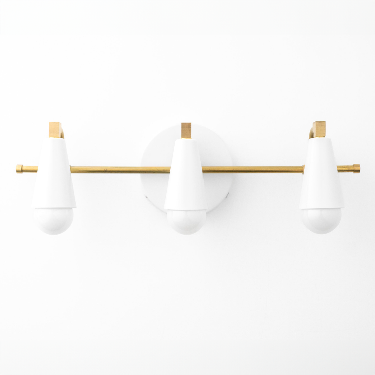 Three white cone-shaped vanity lights with round bulbs mounted on a horizontal brass rod and circular brass wall plate. - VANITY LIGHT MODEL NO. 8084