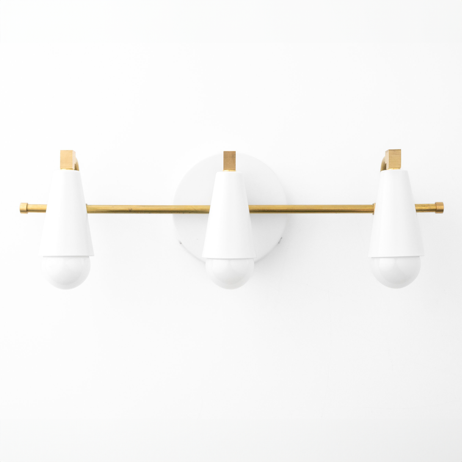 Three white cone-shaped vanity lights with round bulbs mounted on a horizontal brass rod and circular brass wall plate. - VANITY LIGHT MODEL NO. 8084