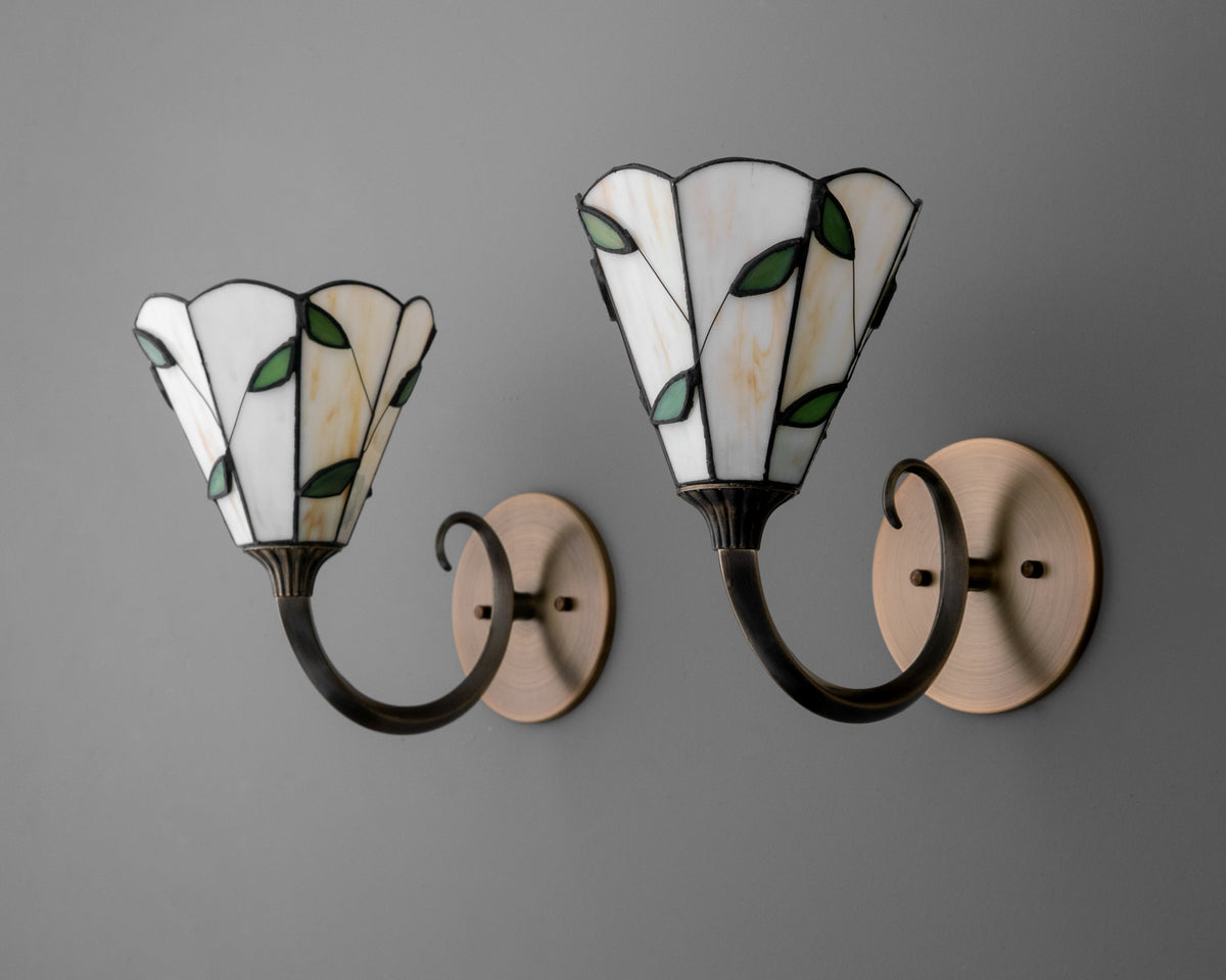 Pair of wall sconces with curved black metal arms and stained glass shades featuring white panels and green leaf accents. - SCONCE MODEL NO. 1056