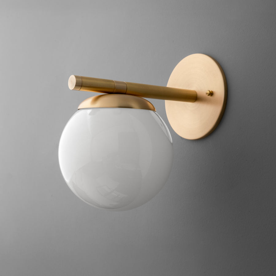 Modern wall sconce with matte white glass globe and raw brass fixture on gray background. - SCONCE MODEL NO. 1358