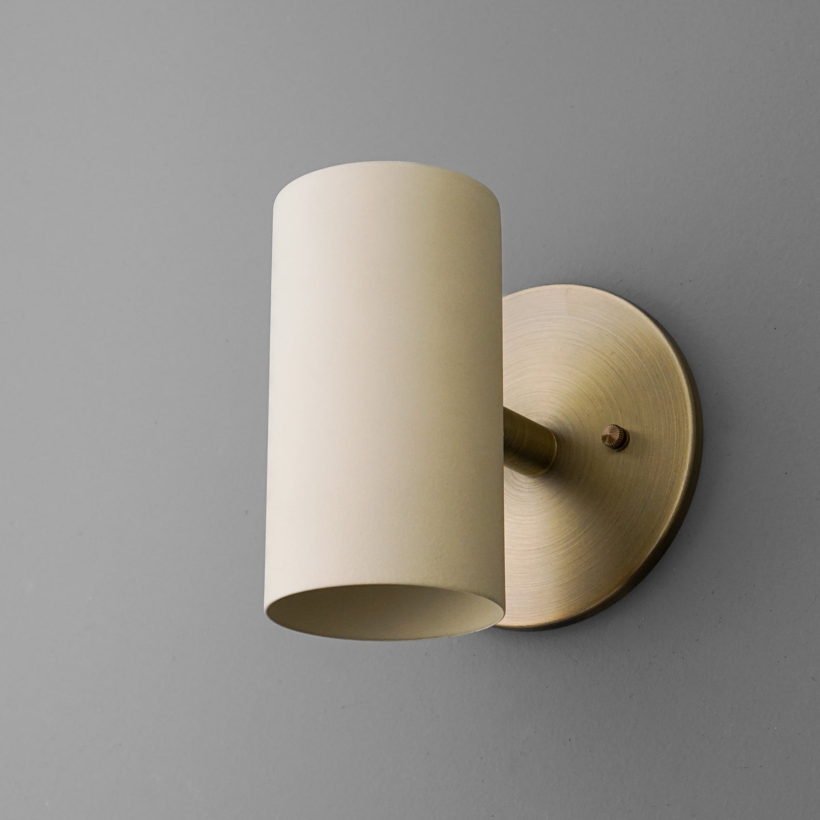 Cylinder sconce with a Cream shade on a short stem from an Antique Brass round wall plate, angled view. - SCONCE MODEL NO. 9697