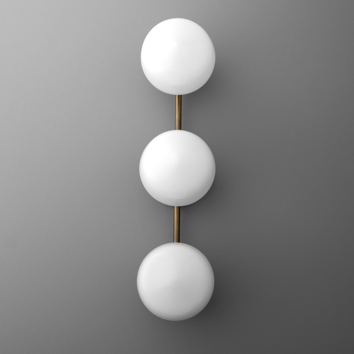 Wall sconce with three frosted white globe lights aligned vertically on a slim brass rod. - SCONCE MODEL NO. 1106