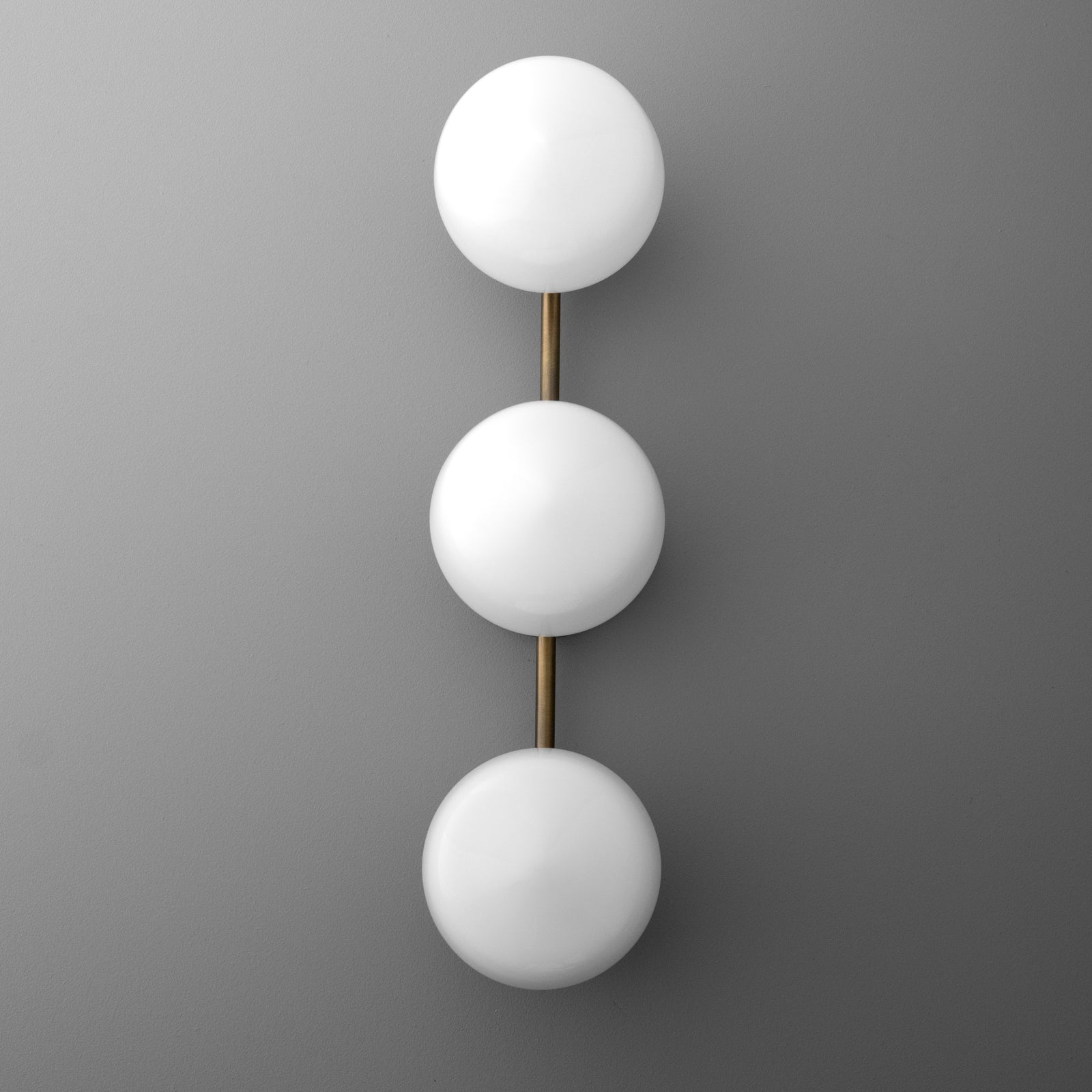 Wall sconce with three frosted white globe lights aligned vertically on a slim brass rod. - SCONCE MODEL NO. 1106