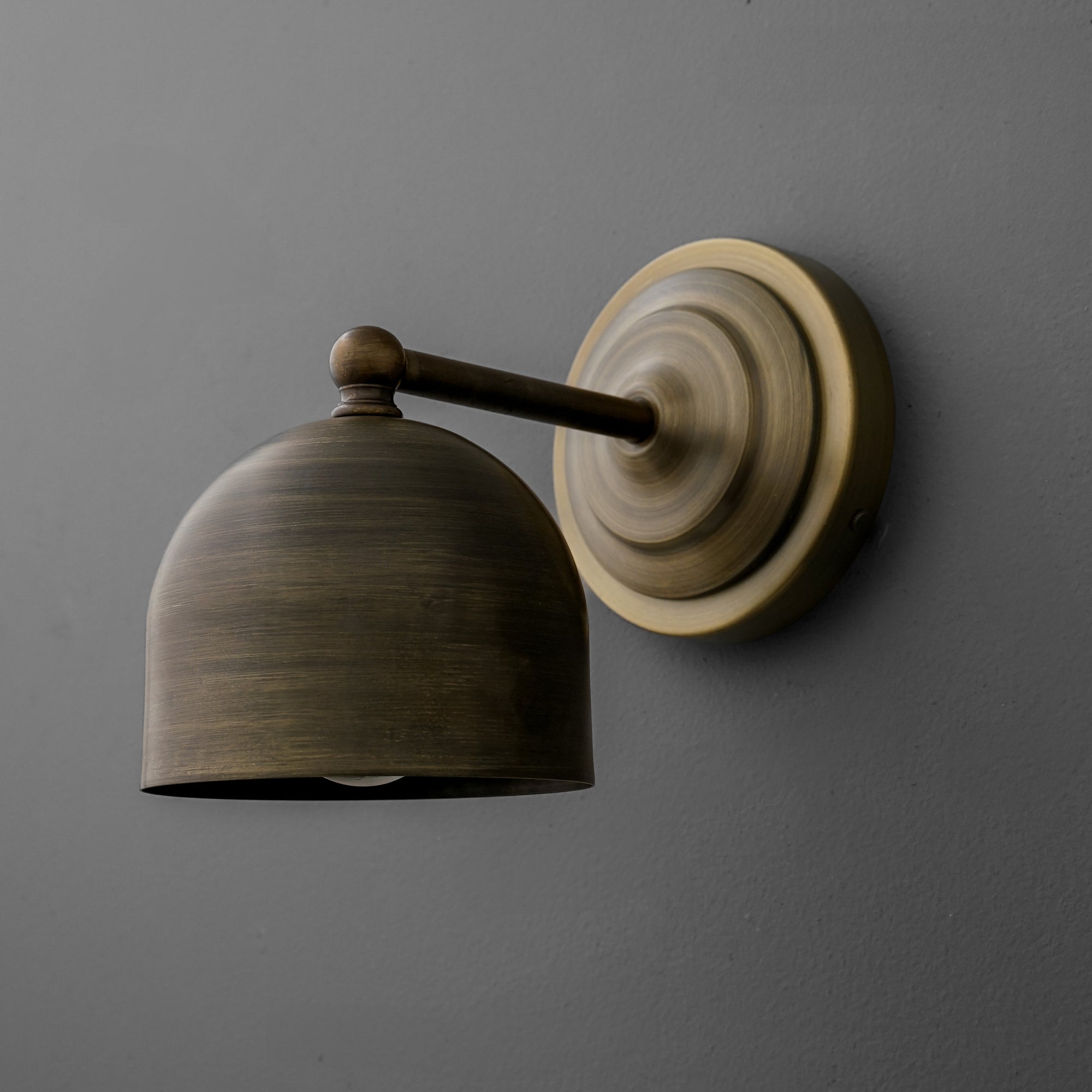 Wall-mounted antique brass sconce with dome-shaped shade and round backplate on gray wall. - SCONCE MODEL NO. 6649