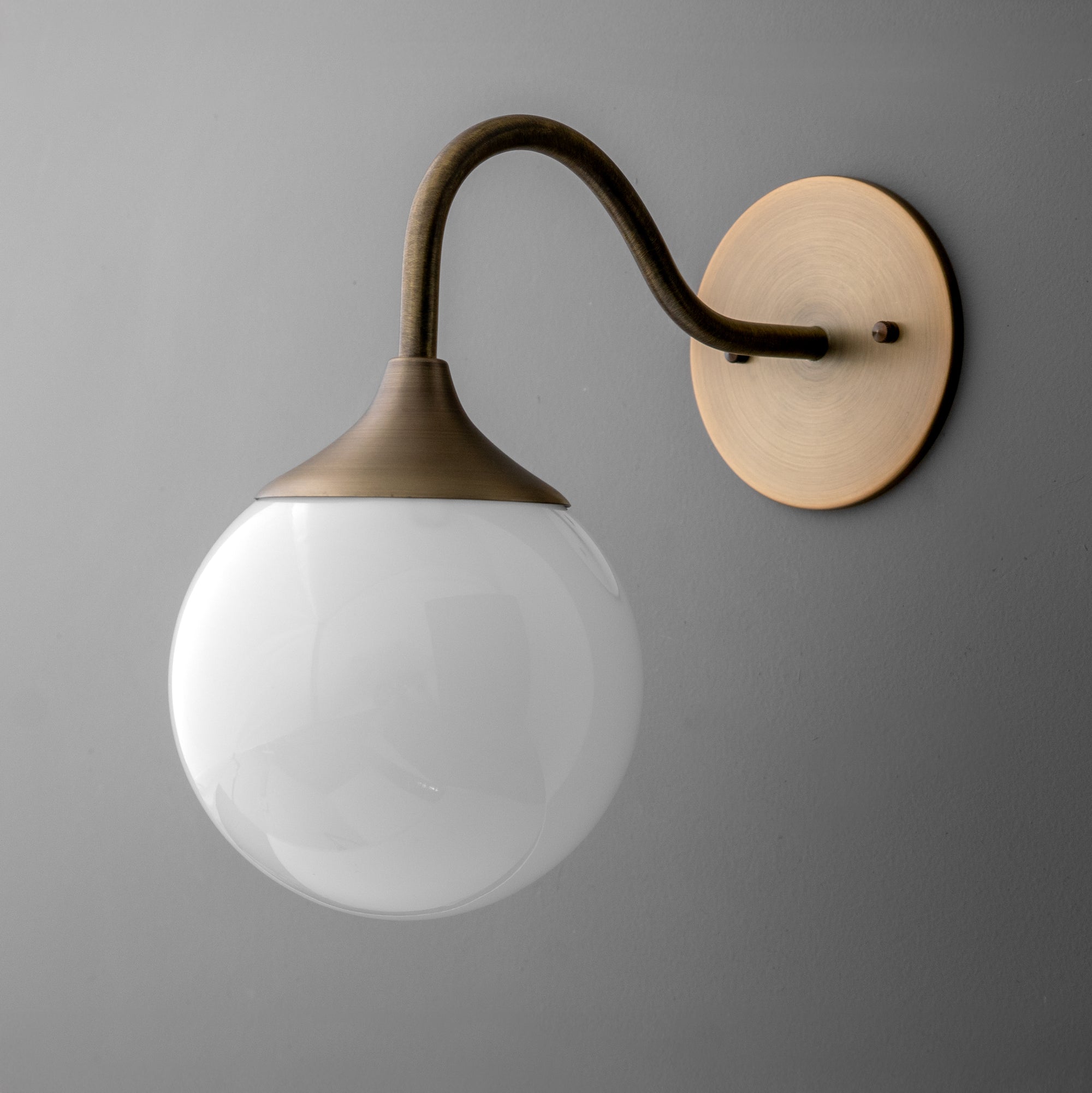 Wall sconce with curved antique brass arm and round frosted glass globe shade on brass backplate. - SCONCE MODEL NO. 8734