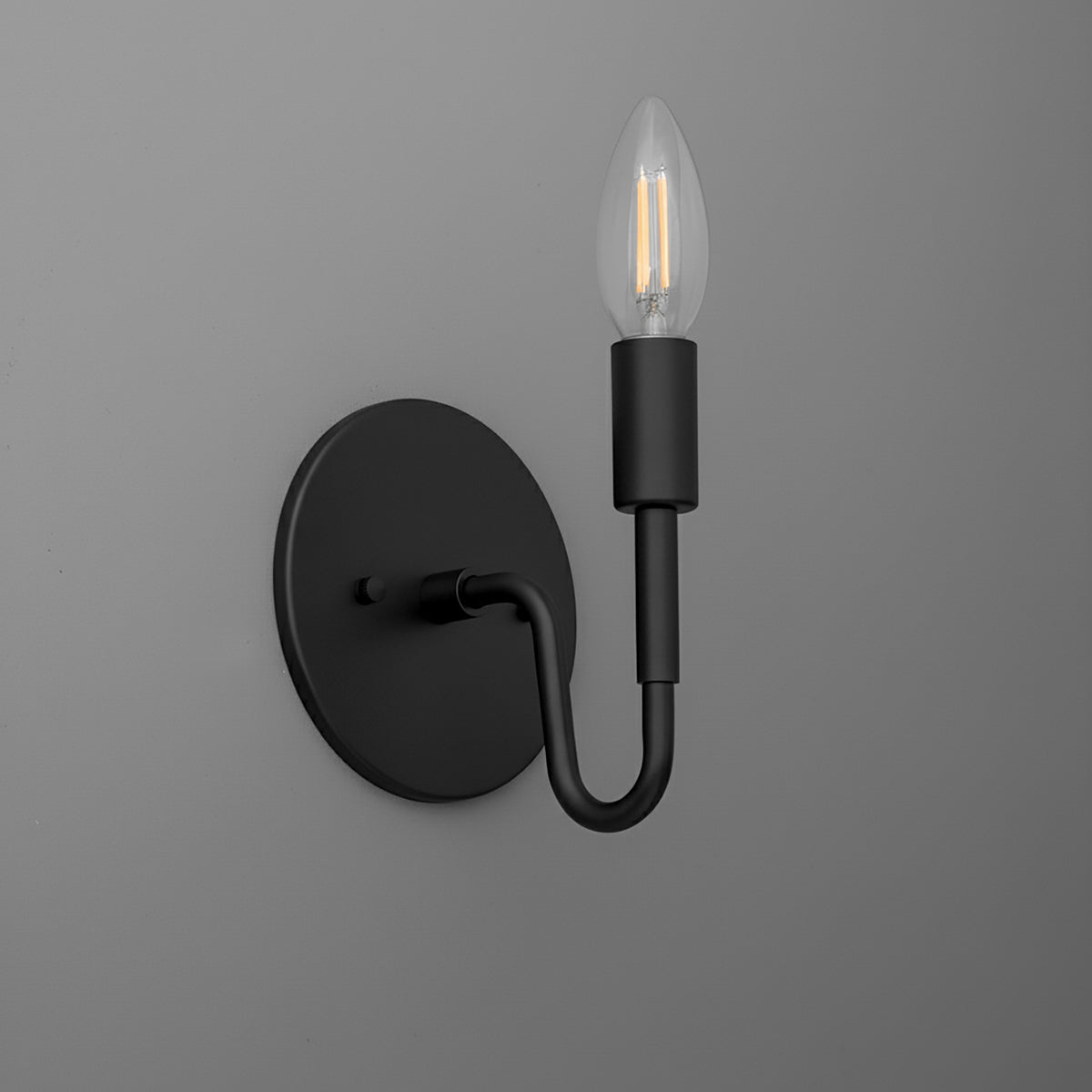 Black metal wall sconce with round base and curved arm holding an exposed bulb. - SCONCE MODEL NO. 1100