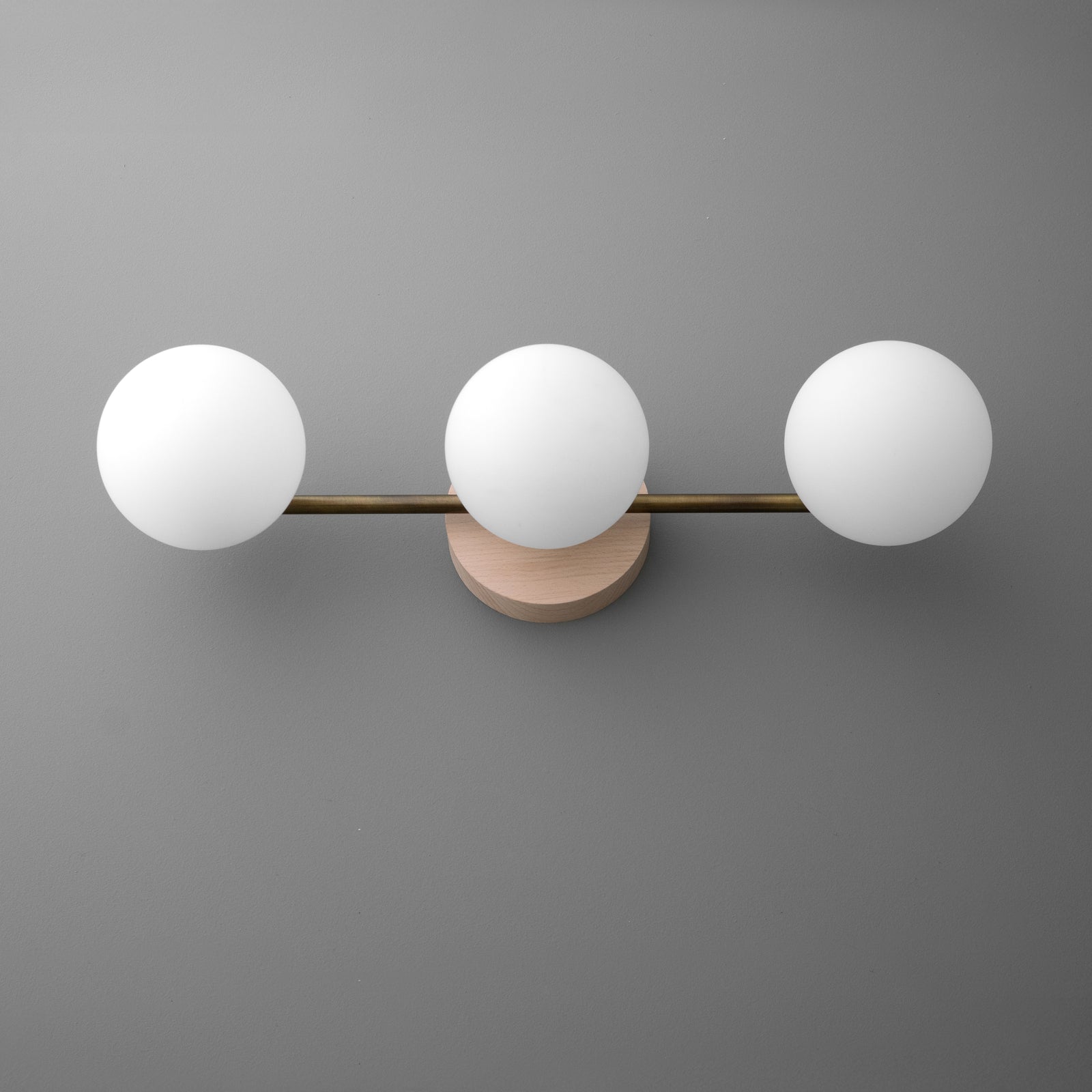 Three white frosted glass globe bulbs on a horizontal brushed brass bar with a round brass wall mount. - VANITY LIGHT MODEL NO. 6089