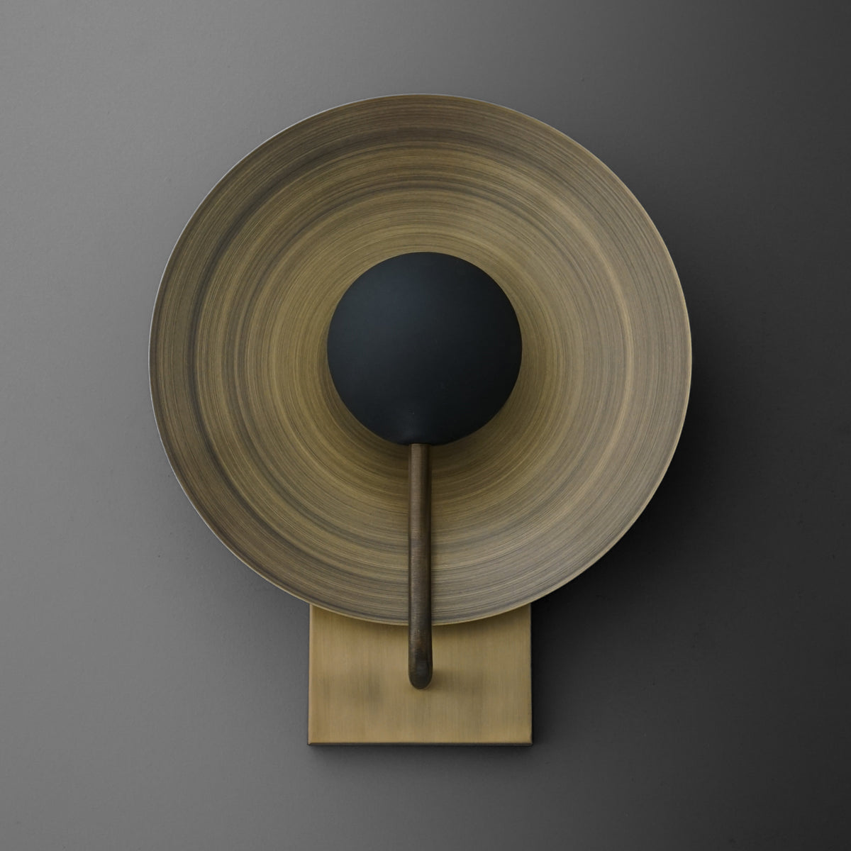 Antique brass wall sconce with a wide, circular backplate and a single black bulb holder centered on a slim arm. - SCONCE MODEL NO. 7858