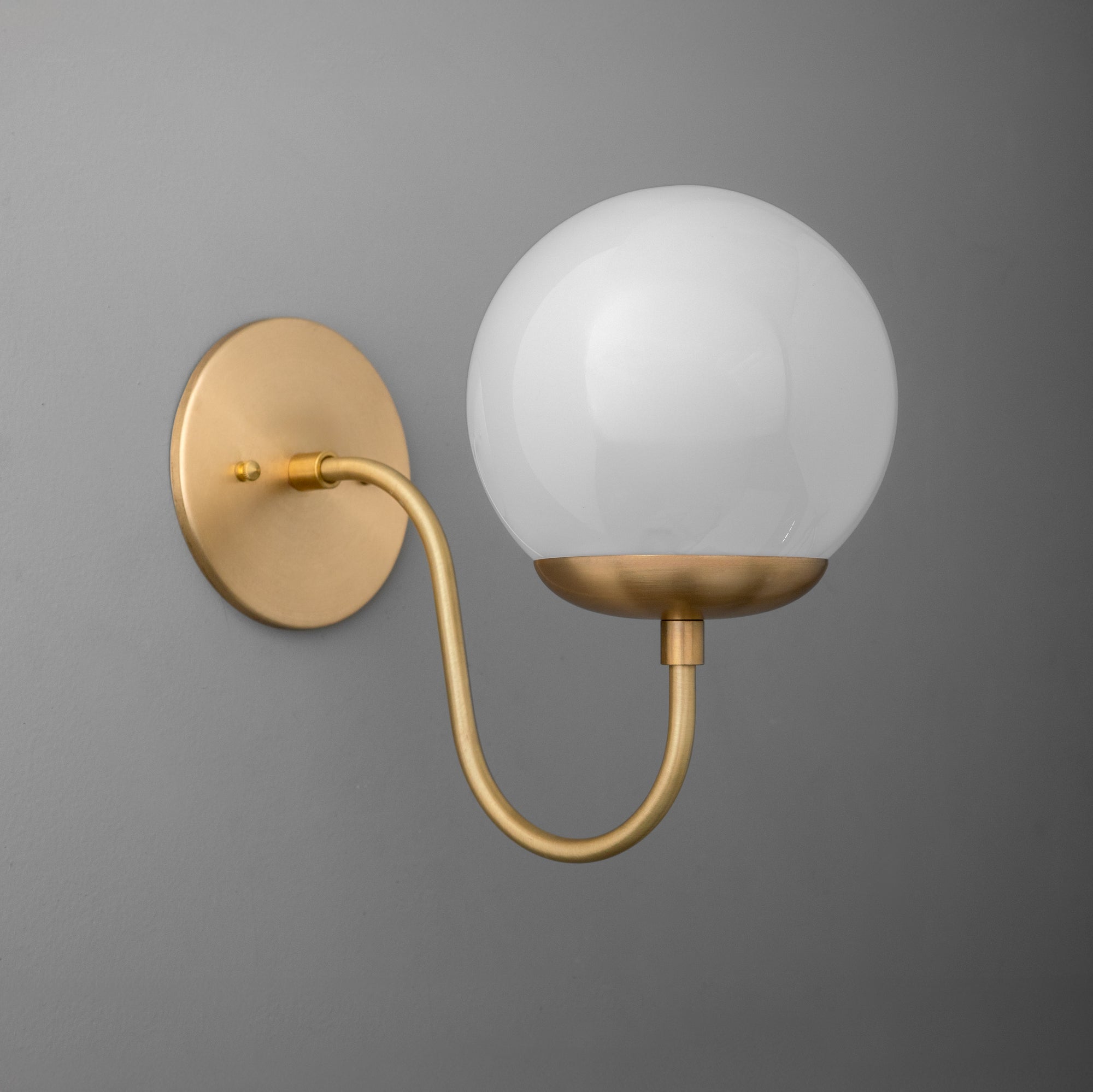 Wall sconce with matte brass finish, curved arm, and frosted glass globe shade. - SCONCE MODEL NO. 3849