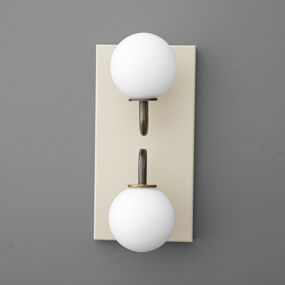 Modern wall sconce with two white frosted glass globes on brass arms mounted on a beige rectangular backplate. - SCONCE MODEL NO. 9868