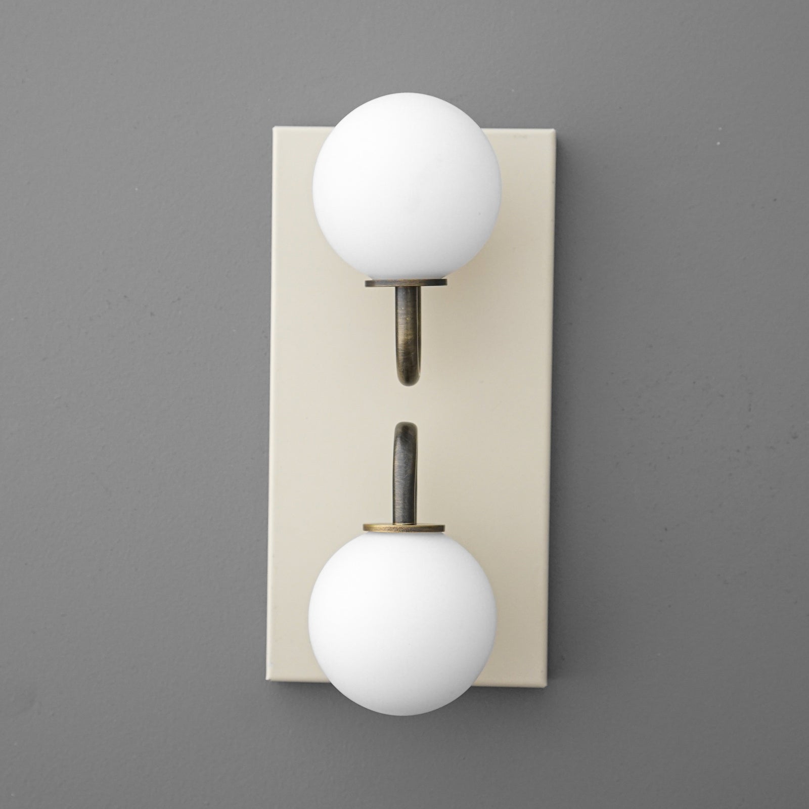 Modern wall sconce with two white frosted glass globes on brass arms mounted on a beige rectangular backplate. - SCONCE MODEL NO. 9868