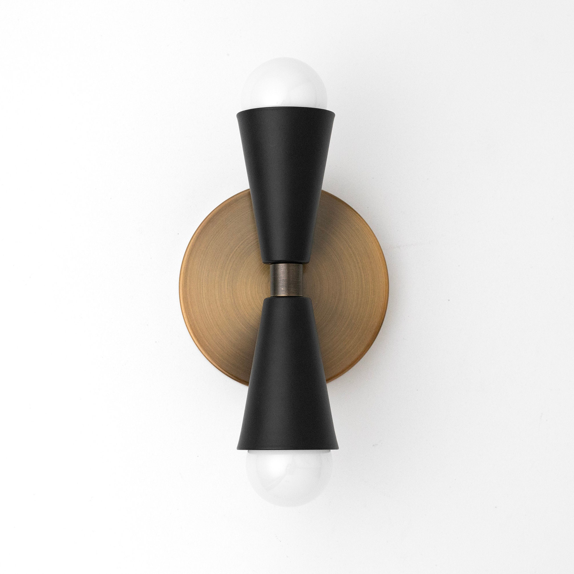 Art Deco wall sconce with black metal tapered cones and two exposed white bulbs, mounted on a round brass base. - SCONCE MODEL NO. 4717