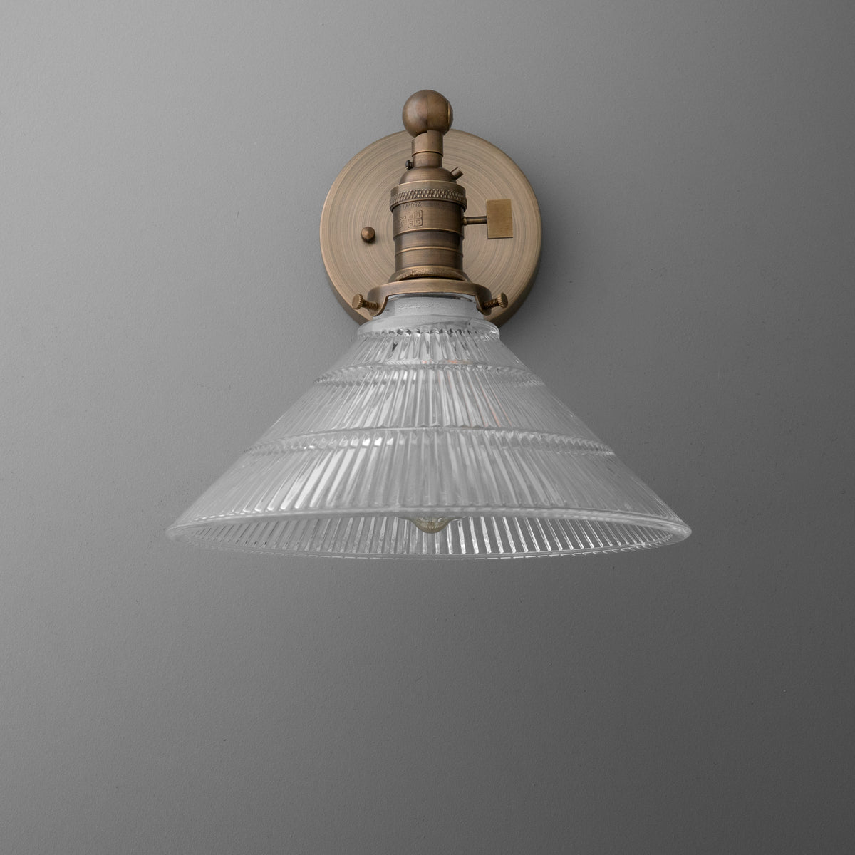Wall-mounted brass sconce with ribbed clear glass conical shade and round backplate. - SCONCE MODEL NO. 3170