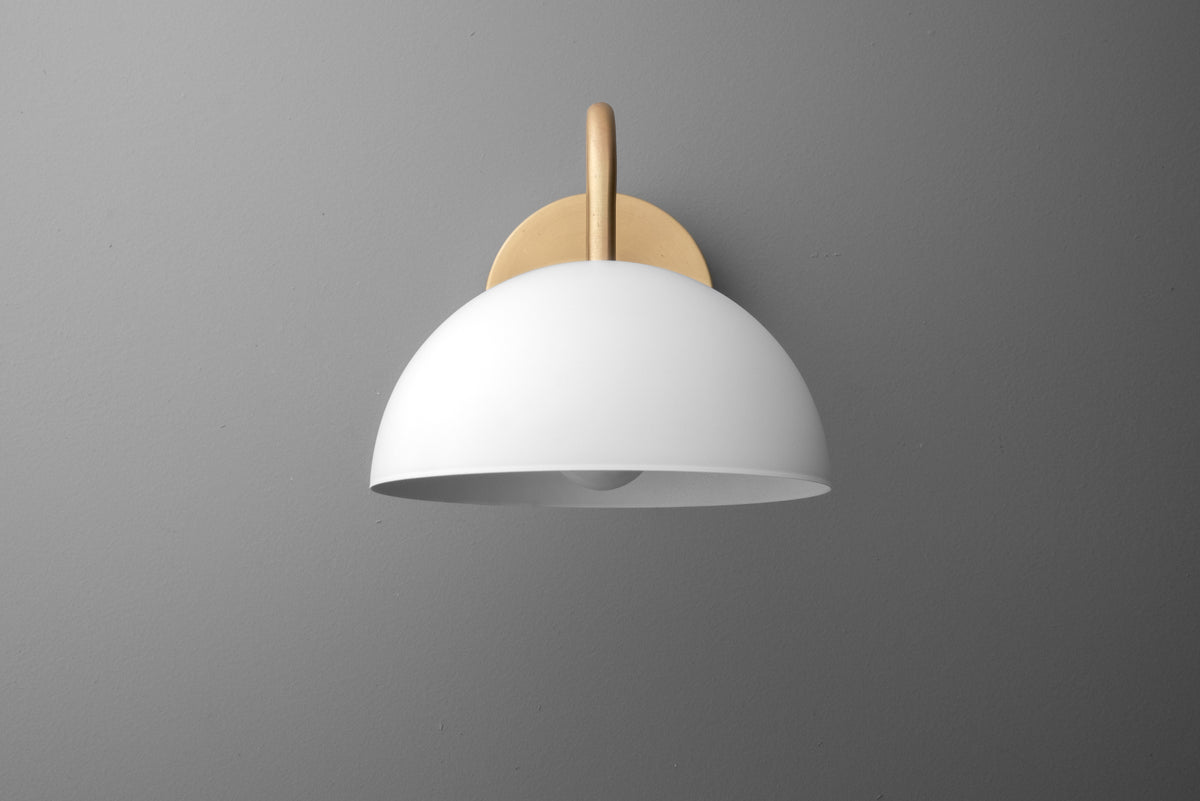 Wall sconce with a smooth, white dome shade and a warm brass mounting plate against a gray background. - SCONCE MODEL NO. 6679